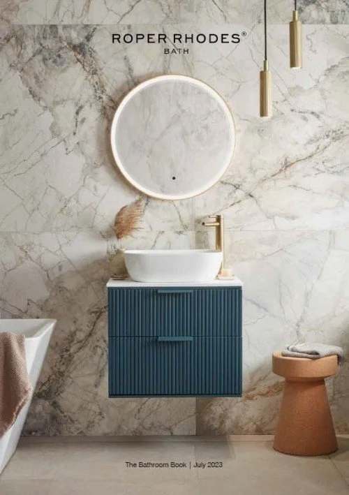 Modern bathroom with marble wall, round mirror, blue vanity with white vessel sink, gold faucet, a towel on bathtub, tan stool with towel, and hanging pendant lights.