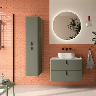 Modern bathroom with green storage cabinet, circular mirror with backlight, and a vessel sink on a green vanity, pink brick wall backdrop, and a hanging pendant light. Colourful vanity unit available at Island Bathrooms Salisbury, Wiltshire