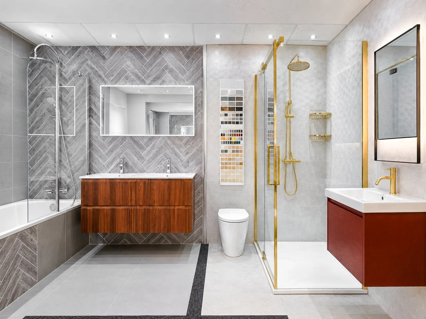 Modern bathroom with gray and white tile walls, a large mirror, a double sink vanity with wooden drawers, a white toilet, a walk-in shower with gold fixtures, and a bathtub with a glass divider.