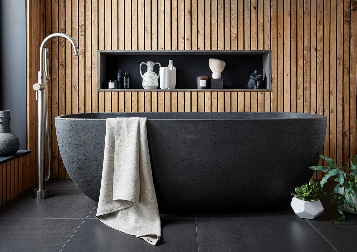 Modern bathroom with a black bathtub, wooden wall paneling, and decorative vases on a built-in shelf