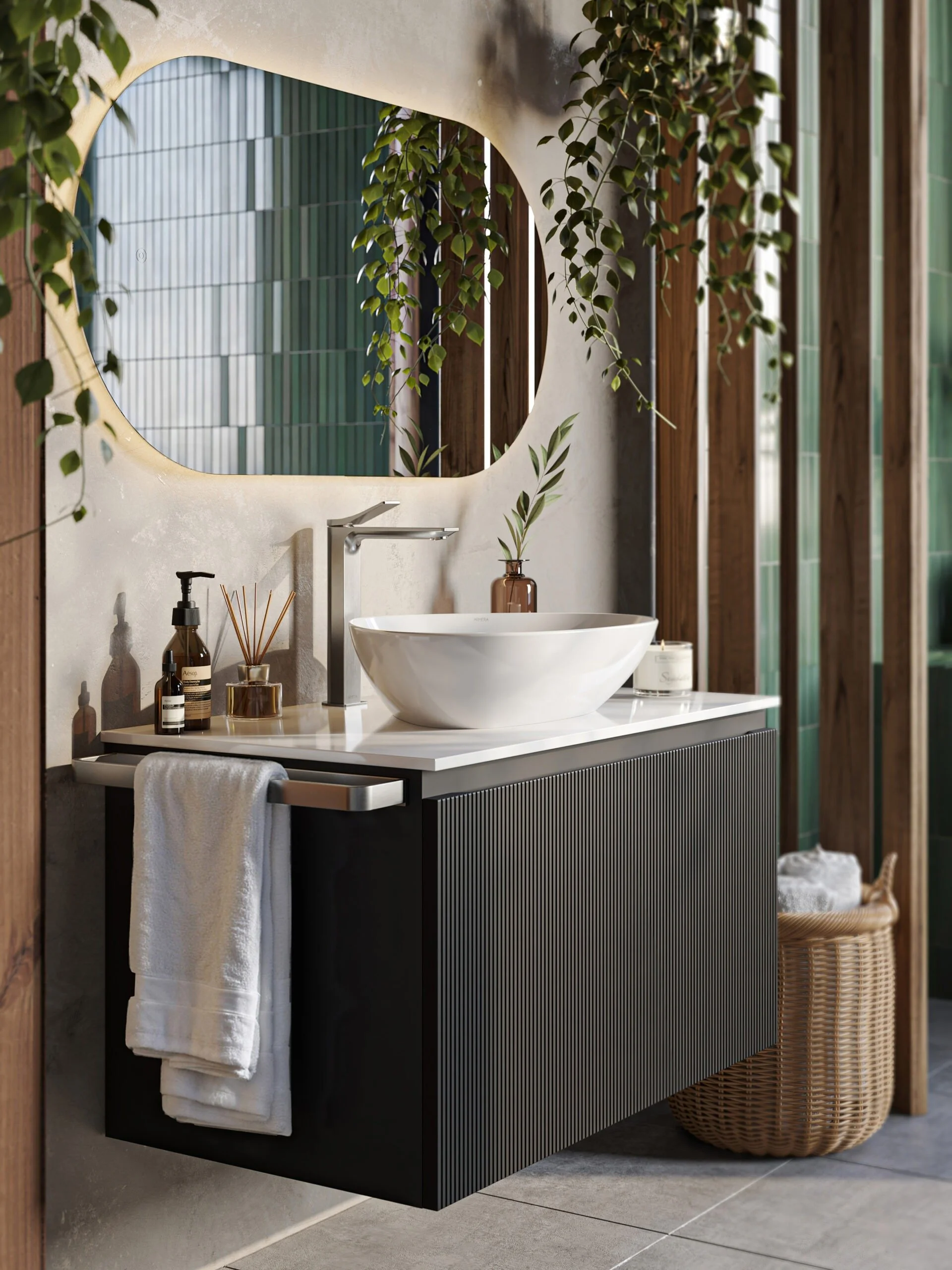 A modern bathroom vanity area with a white ceramic vessel sink, a sleek silver faucet, and a black textured cabinet. A mirror with an irregular shape is mounted on the wall, surrounded by green hanging plants. Island Bathrooms showroom in Dorset.
