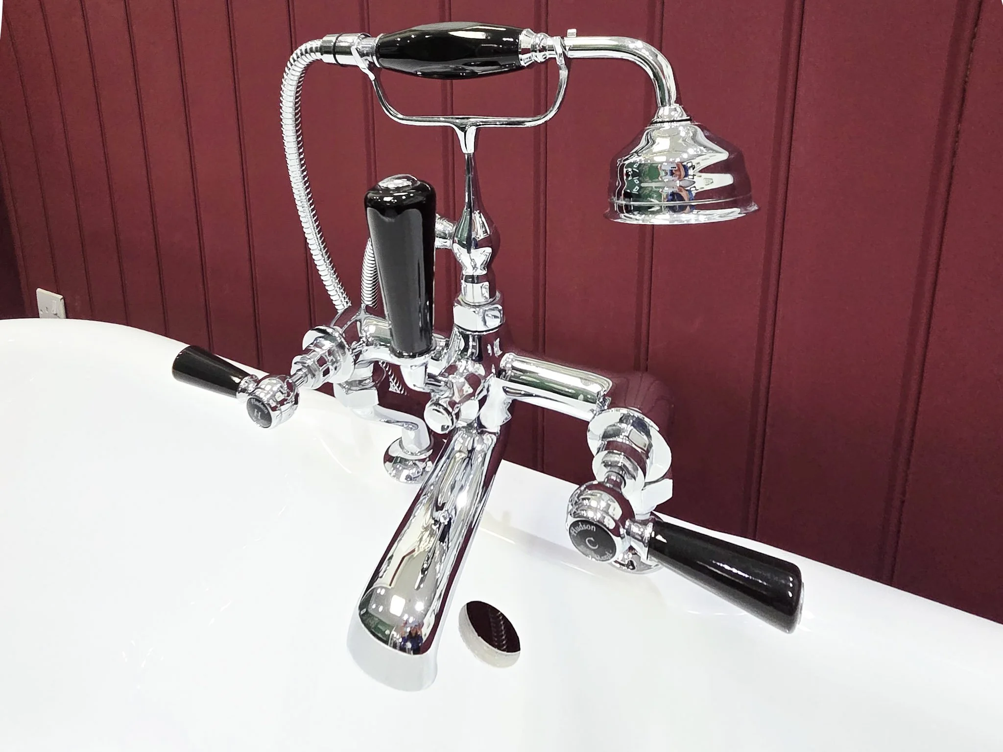 A vintage-style chrome faucet with a mounted handheld shower head on a white sink, against a red wooden paneled wall.