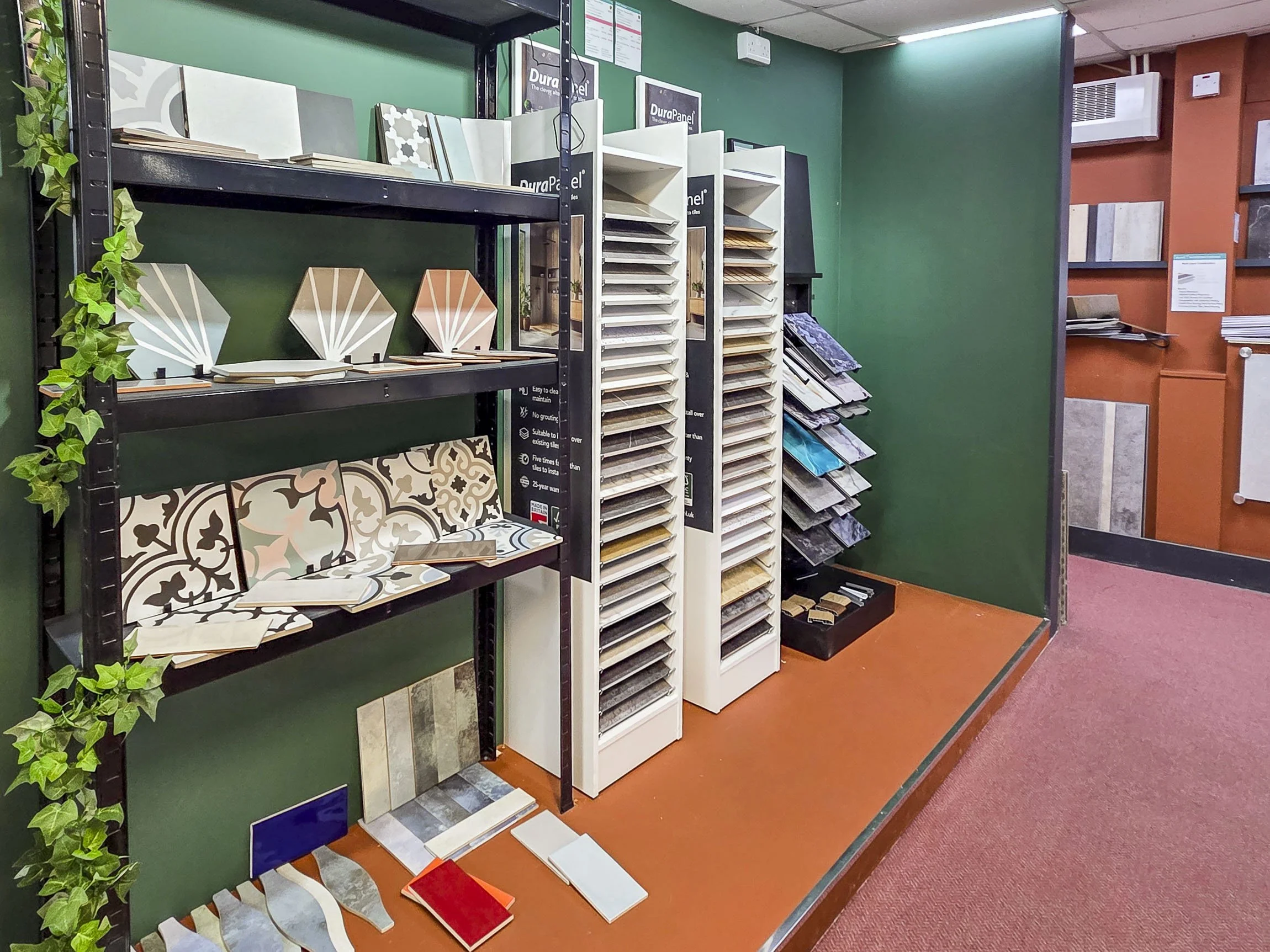 Display of various tile samples and catalogs in a tile showroom, with a green wall background and shelves holding tile pieces and color samples.