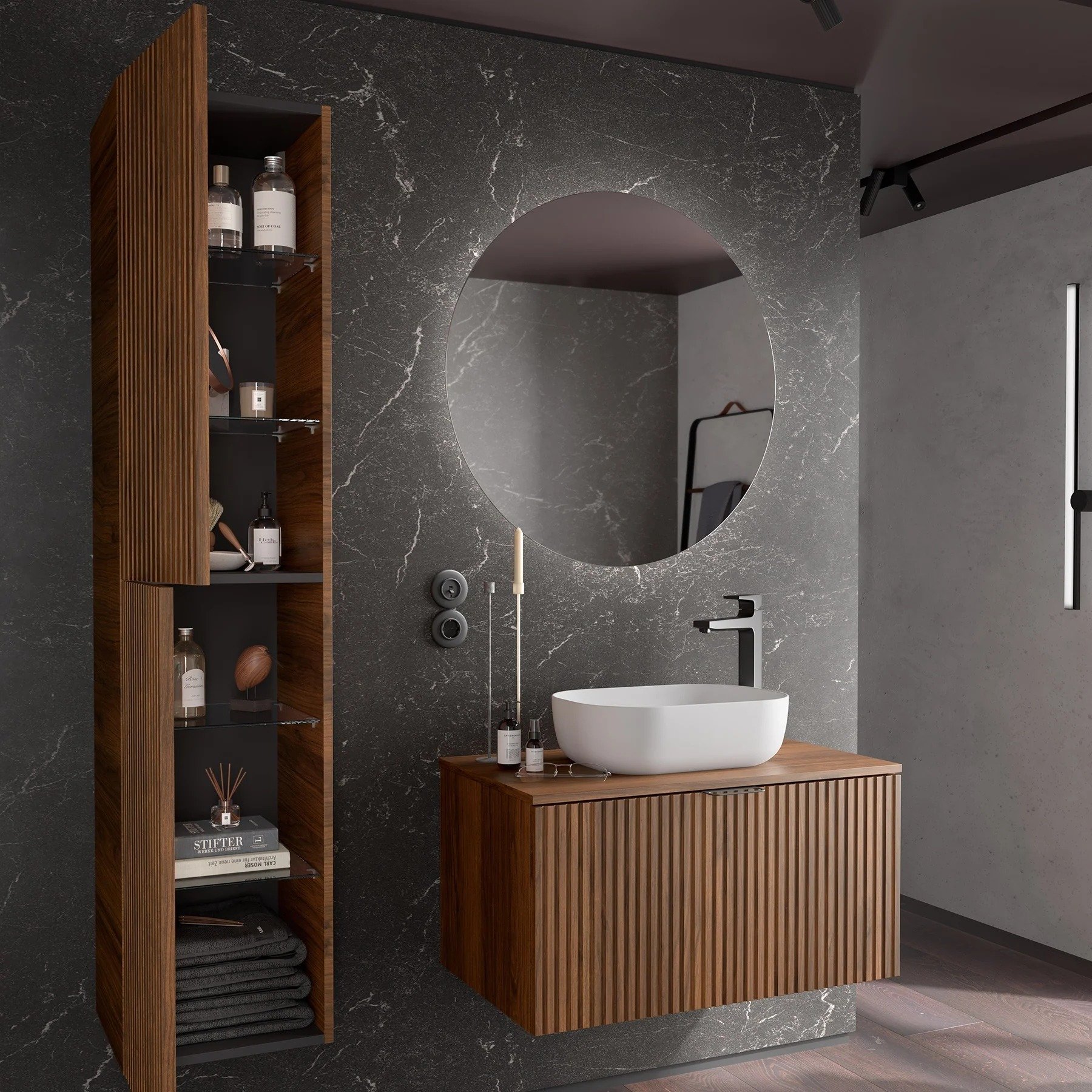 A modern bathroom with a black marble wall, a large round mirror, contemporary bathroom with dark furniture and patterned floor tiles. Bathroom furniture and brassware available at Island Bathrooms Salisbury
