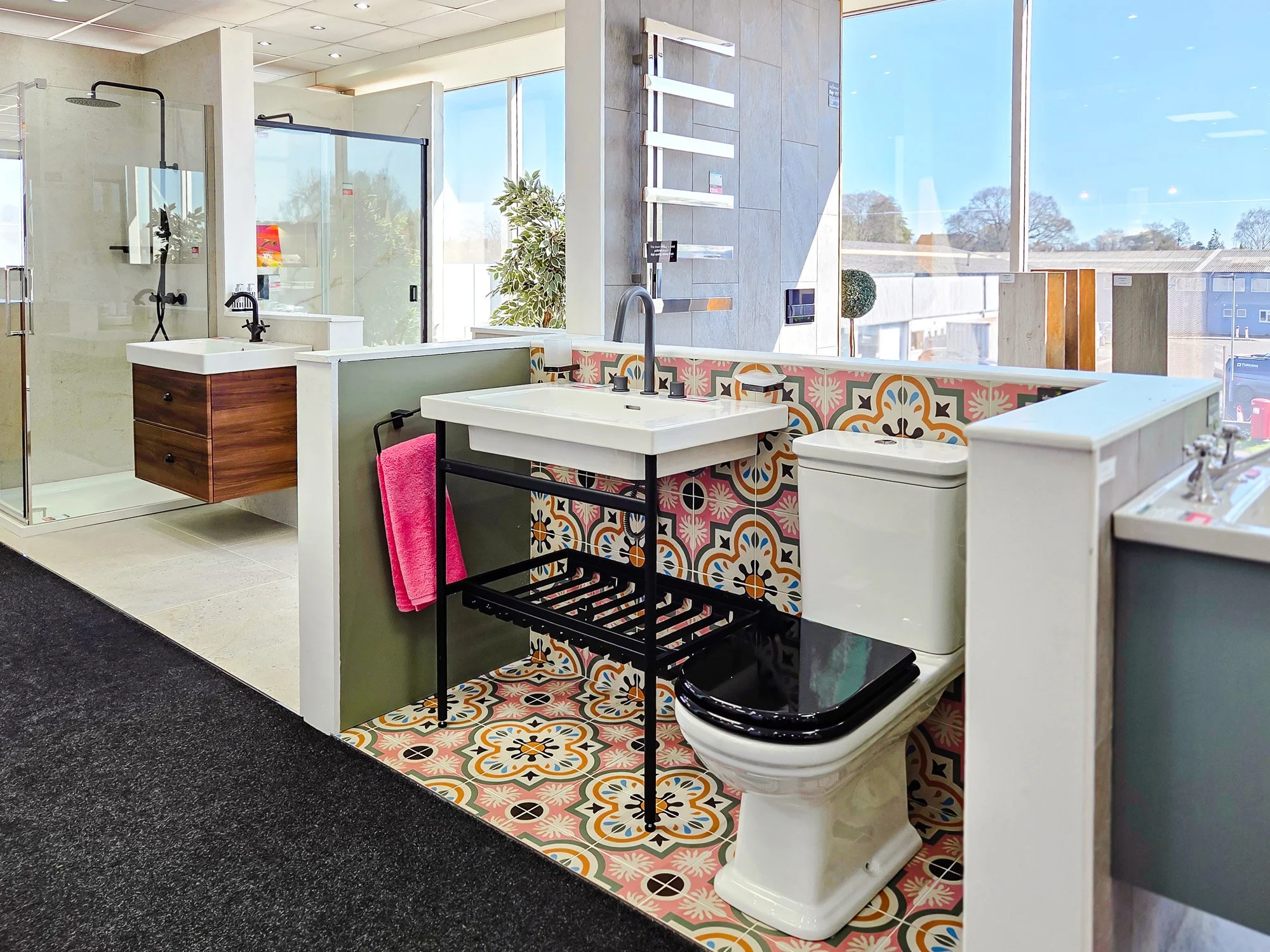 Bathroom display in a store with a walk-in shower, sink, toilet, decorative tile, and large windows showing a clear sky.