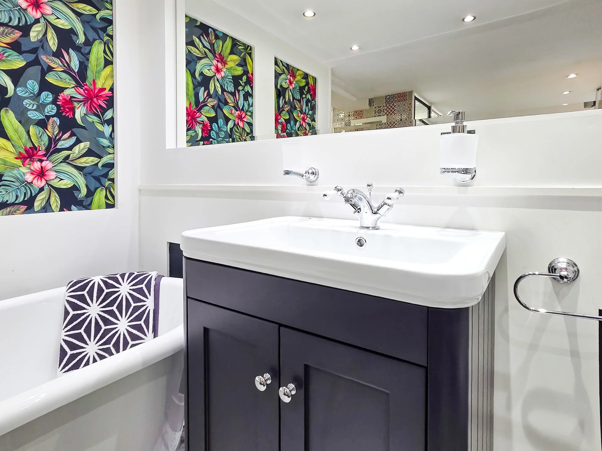 A bathroom with a modern white sink and dark cabinet, decorated with colorful floral wallpaper and a patterned towel hanging on the side.
