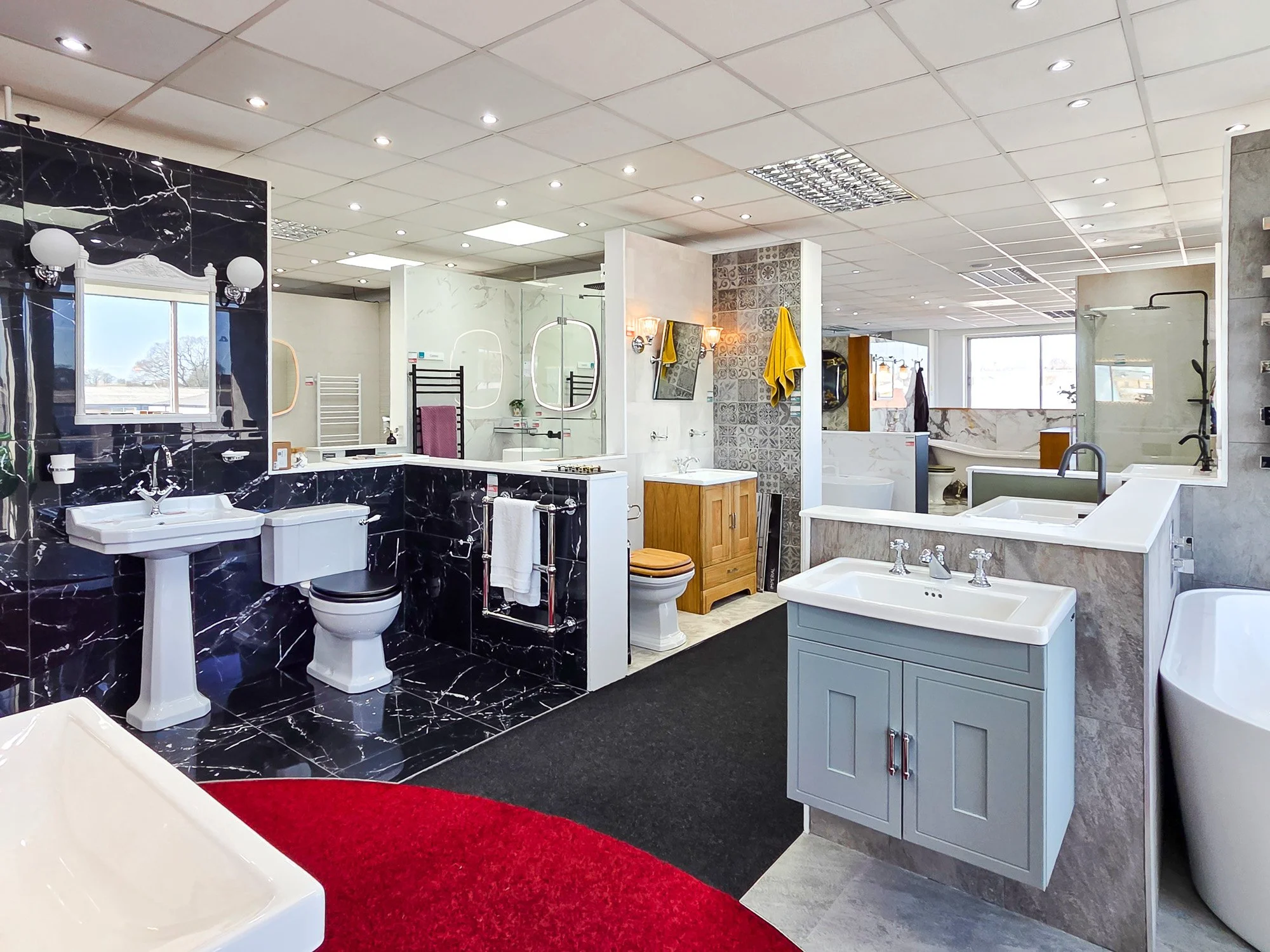 Interior of a bathroom showroom displaying various bathroom fixtures including sinks, toilets, and bathtubs with decorative wall tiles and lighting.