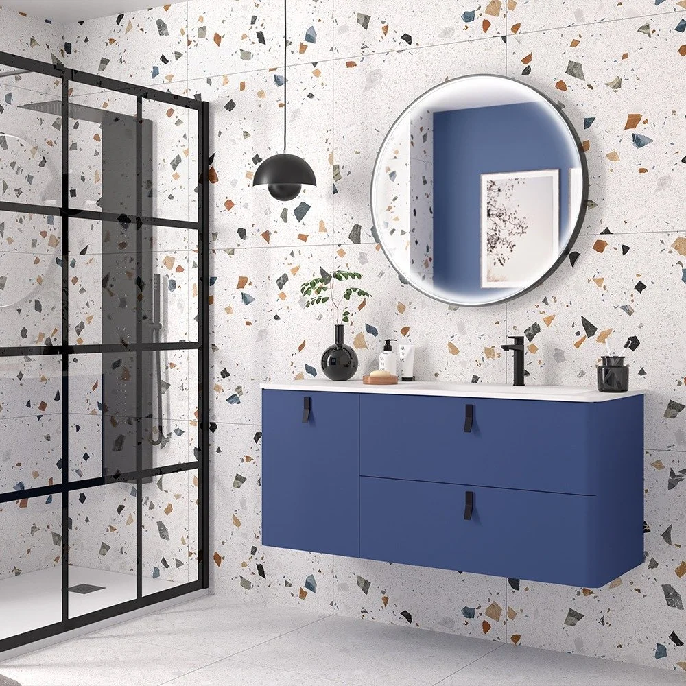 Modern bathroom with terrazzo walls, a black-framed glass shower, a blue floating vanity with black hardware, a round mirror with LED light, and black pendant lighting. Blue vanity unit with brass handles on display at Island Bathrooms Salisbury