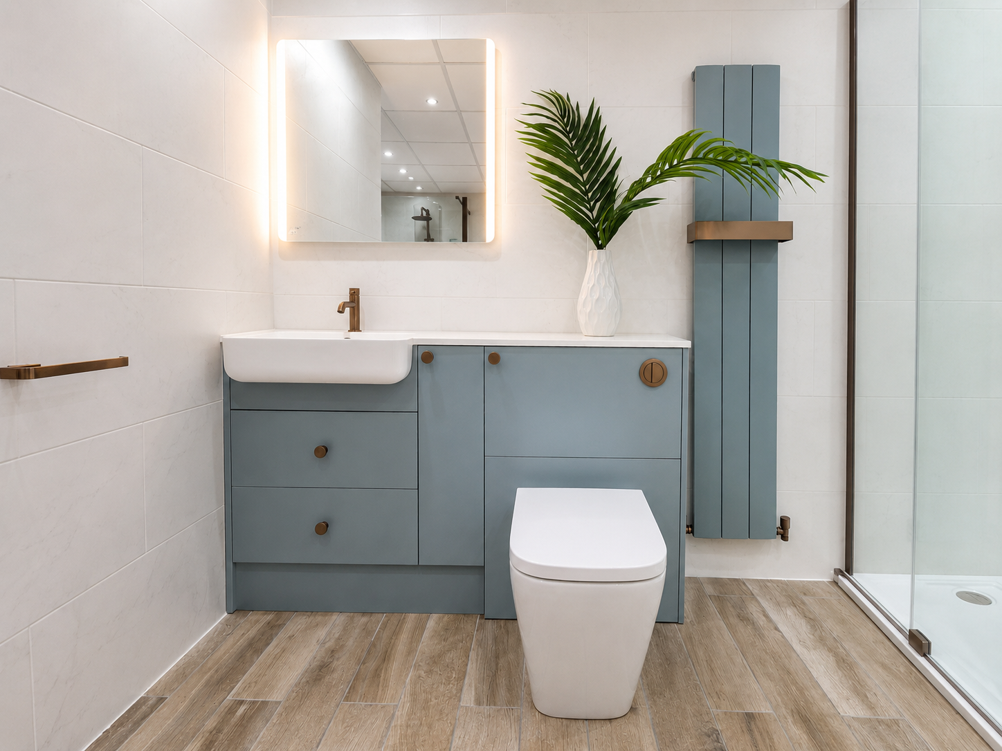 Modern bathroom with blue cabinetry, white sink, large mirror with LED lighting, potted plant, and walk-in shower with glass door.