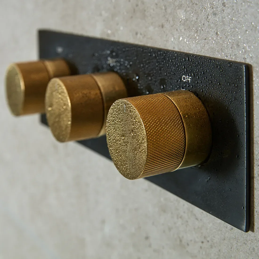 Close-up of a black stove with three gold-colored control knobs, with water droplets on the knobs and the surface.