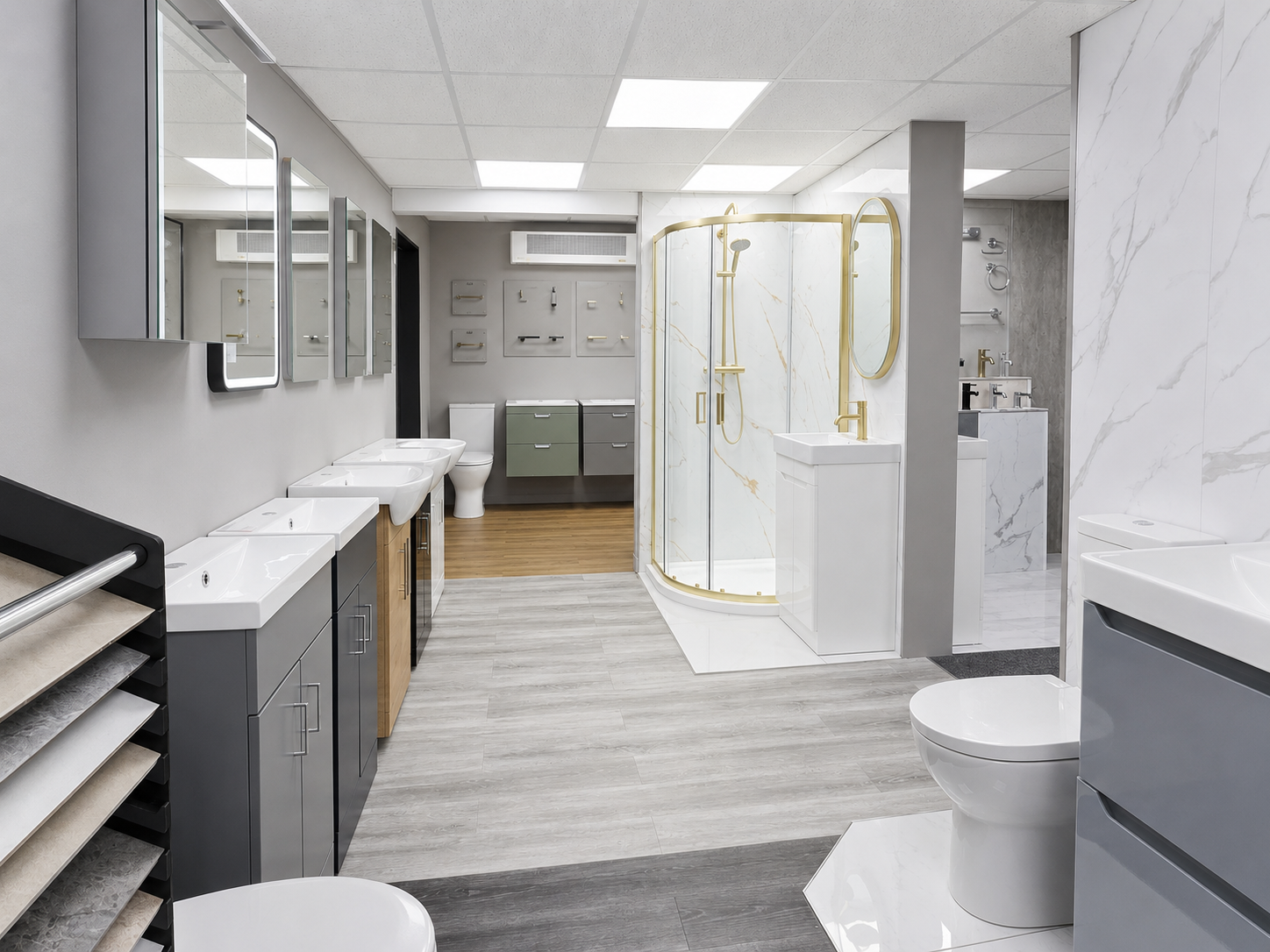 Showroom bathroom with multiple sinks, mirrors, a shower with gold fixtures, and a toilet. Features modern design with light gray, white, and gold accents.