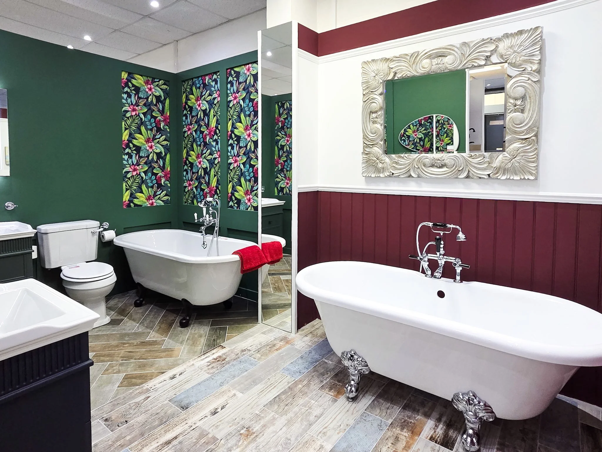A bathroom with vintage clawfoot bathtub, floral wallpaper, ornate mirror, and colorful tile flooring.
