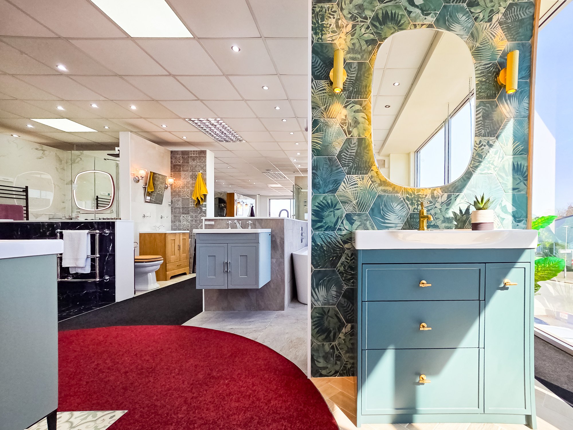 Interior of a bathroom or salon with a decorative leafy wallpaper, large mirror, sink, blue cabinet, and various fixtures and furnishings.