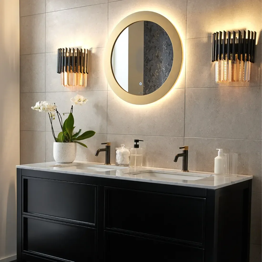 Modern bathroom with double vanity, circular mirror with backlight, wall sconces, potted orchid, soap dispenser, and toothbrush holder.