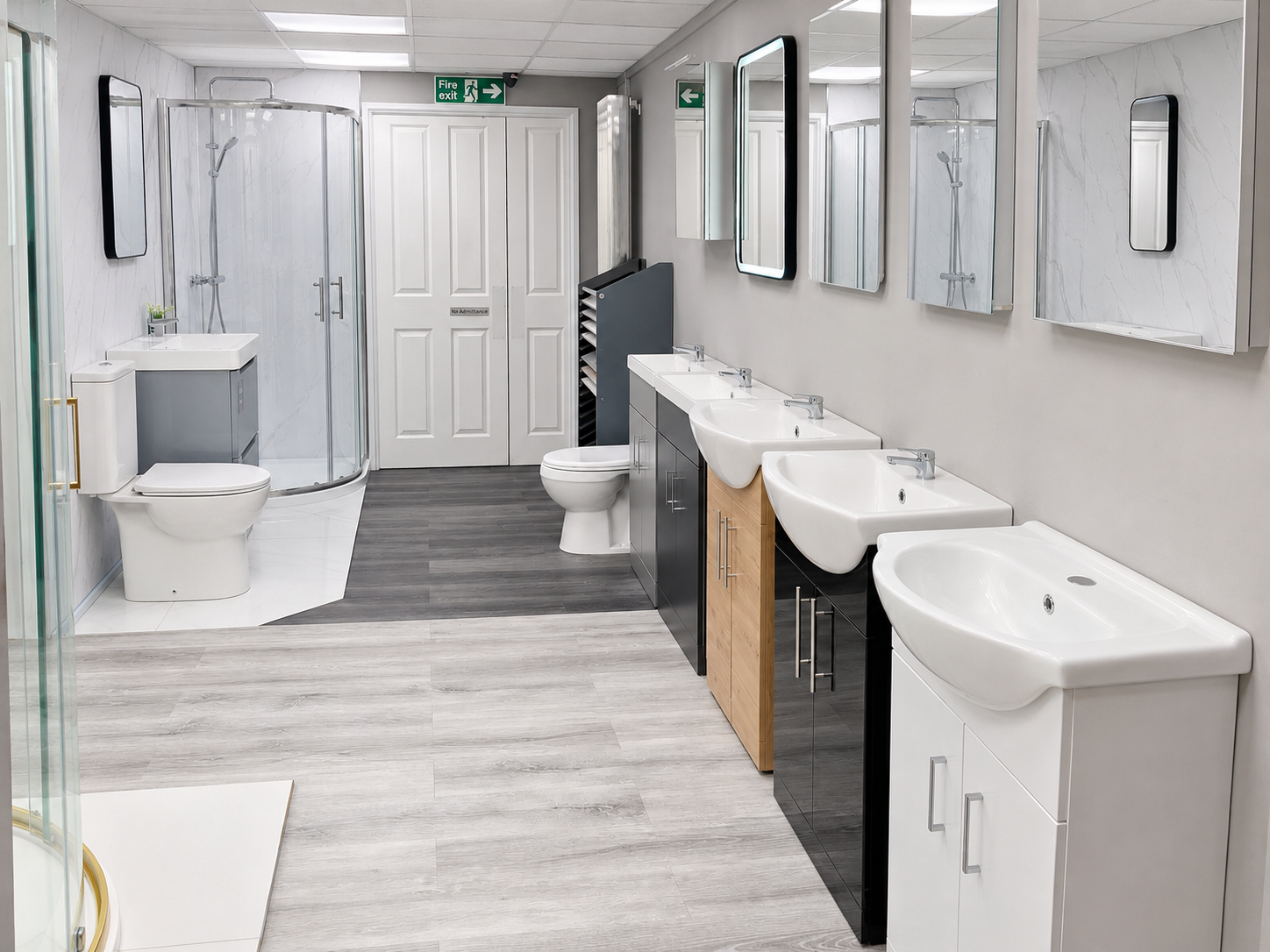 Modern public restroom with multiple sinks, mirrors, toilets, and a shower area, featuring light-colored walls and dark wood flooring.