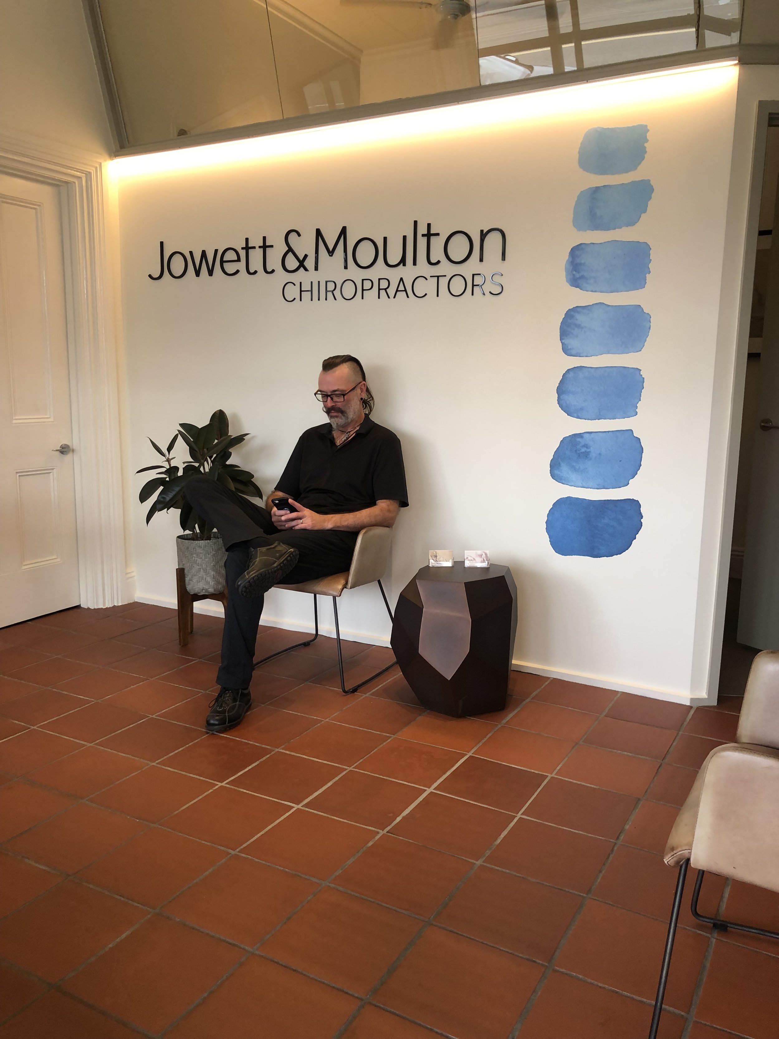 A patient waits in the lobby at our new chiropractic practice in Melbourne - Text on the sign reads Jowett and Moulton Chiropractors Melbourne