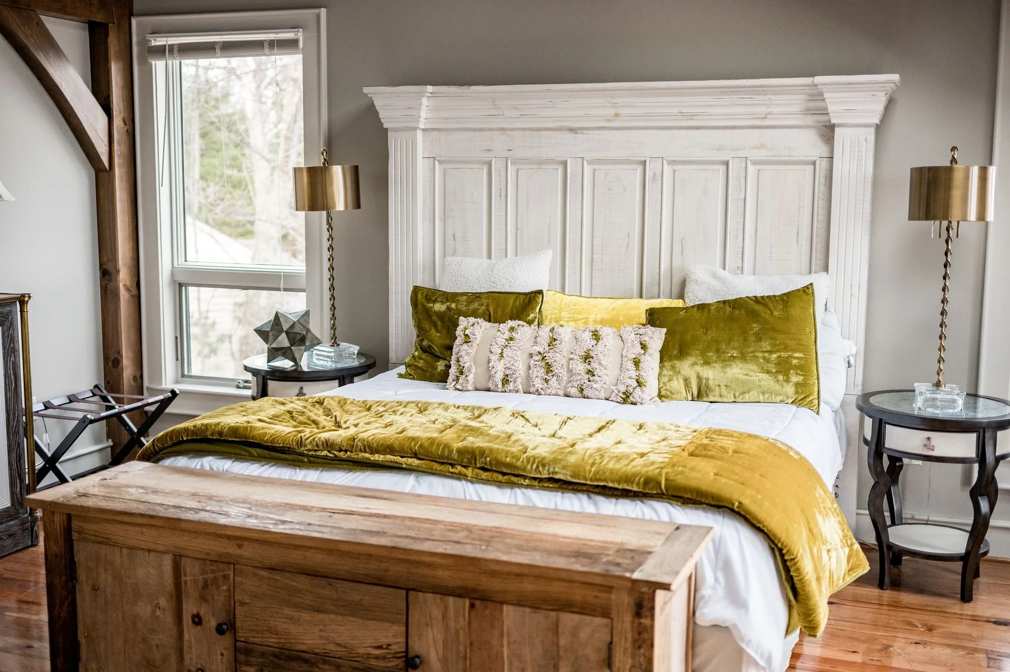 Bedroom with a rustic wood headboard, yellow and green bedding, side tables with glass decor, and brass lamps.