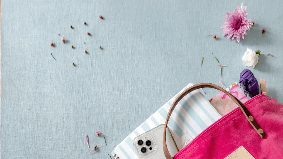 Pink handbag with flowers, smartphone, notebook on a textured blue surface.