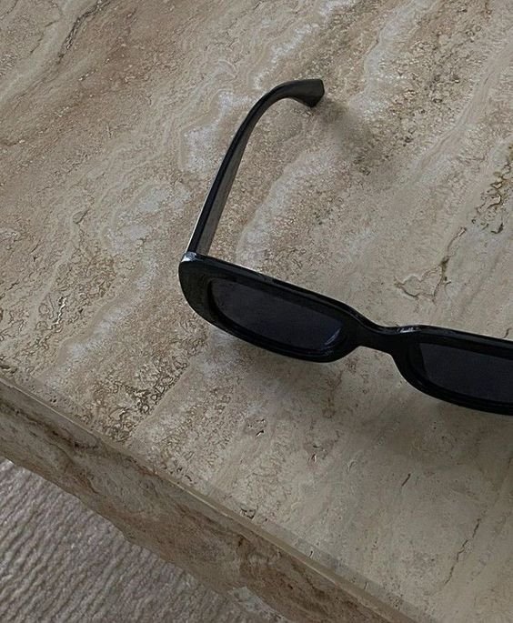 Black rectangular sunglasses on a beige marble table.