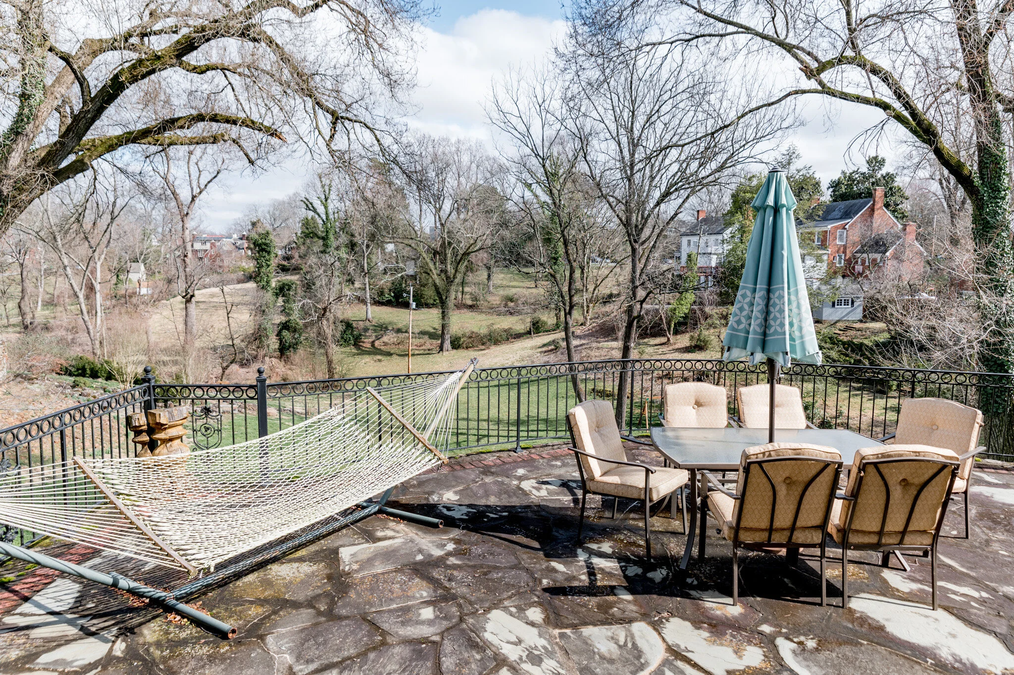 Outdoor patio with a table and chairs, hammock, and umbrella, overlooking a grassy landscape and trees.