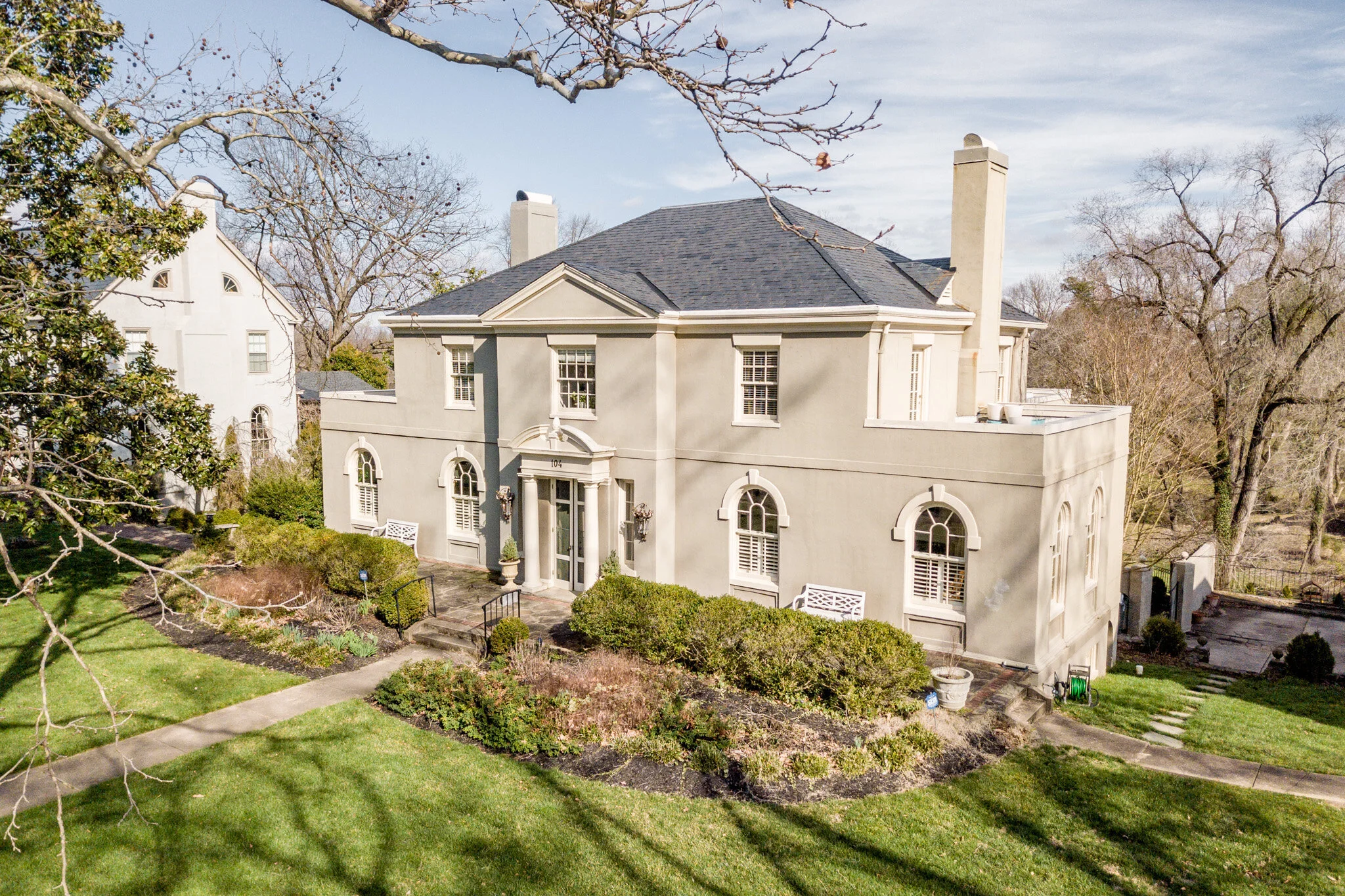 Elegant two-story mansion with arched windows, landscaped garden, and paved entrance path.
