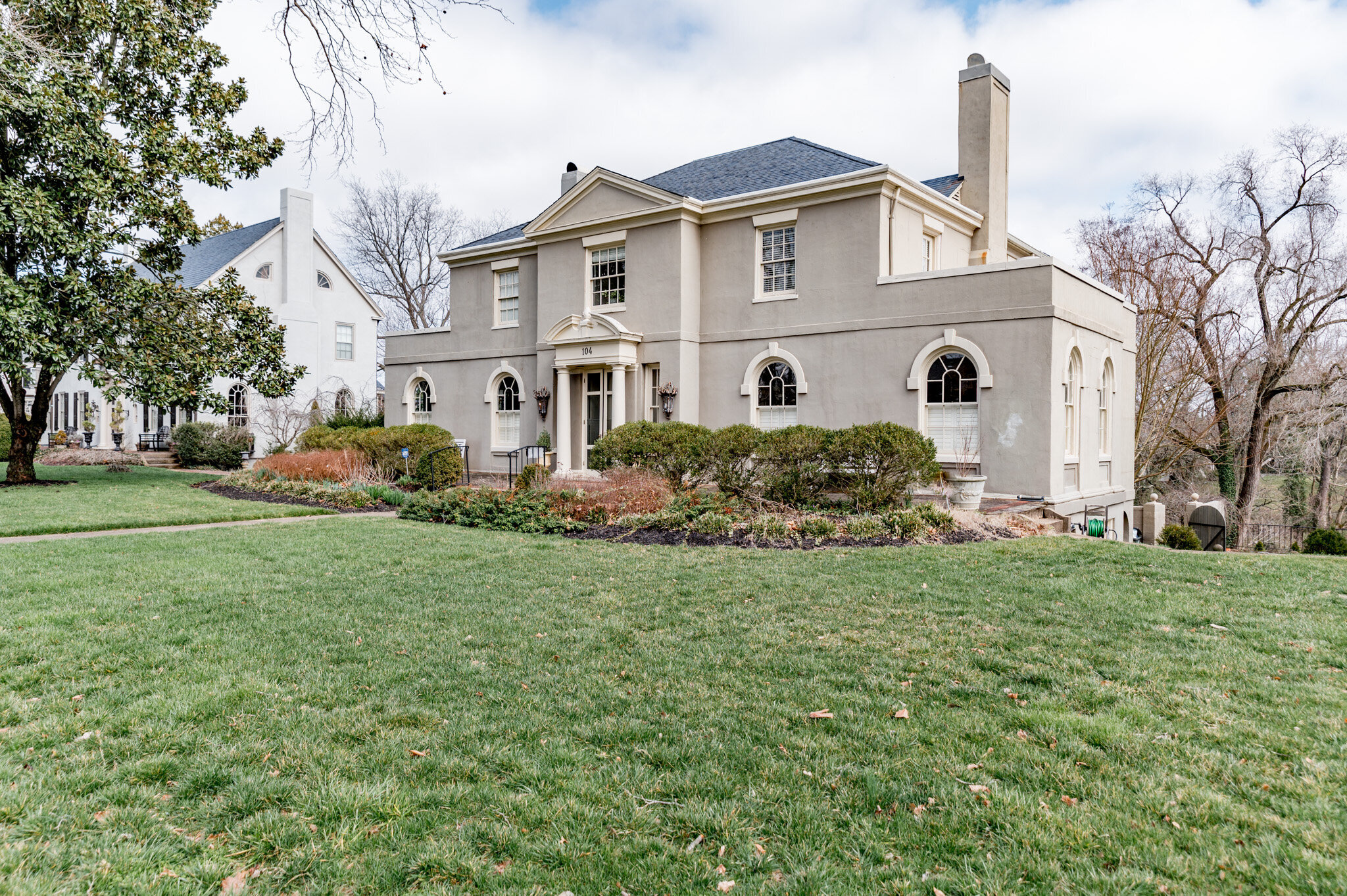 Large beige two-story house with arched windows, surrounded by a well-maintained lawn and trees.