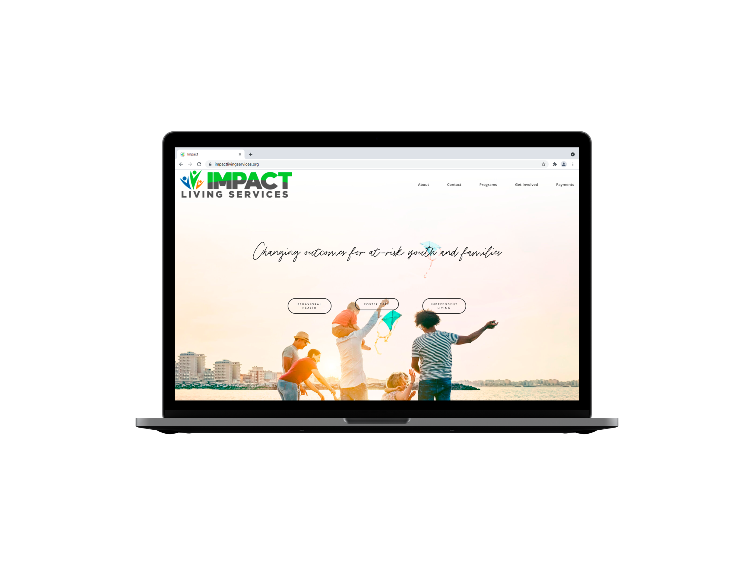 Laptop displaying a website for Impact Living Services, featuring an image of people holding kites on a beach and the slogan "Changing outcomes for at-risk youth and families."
