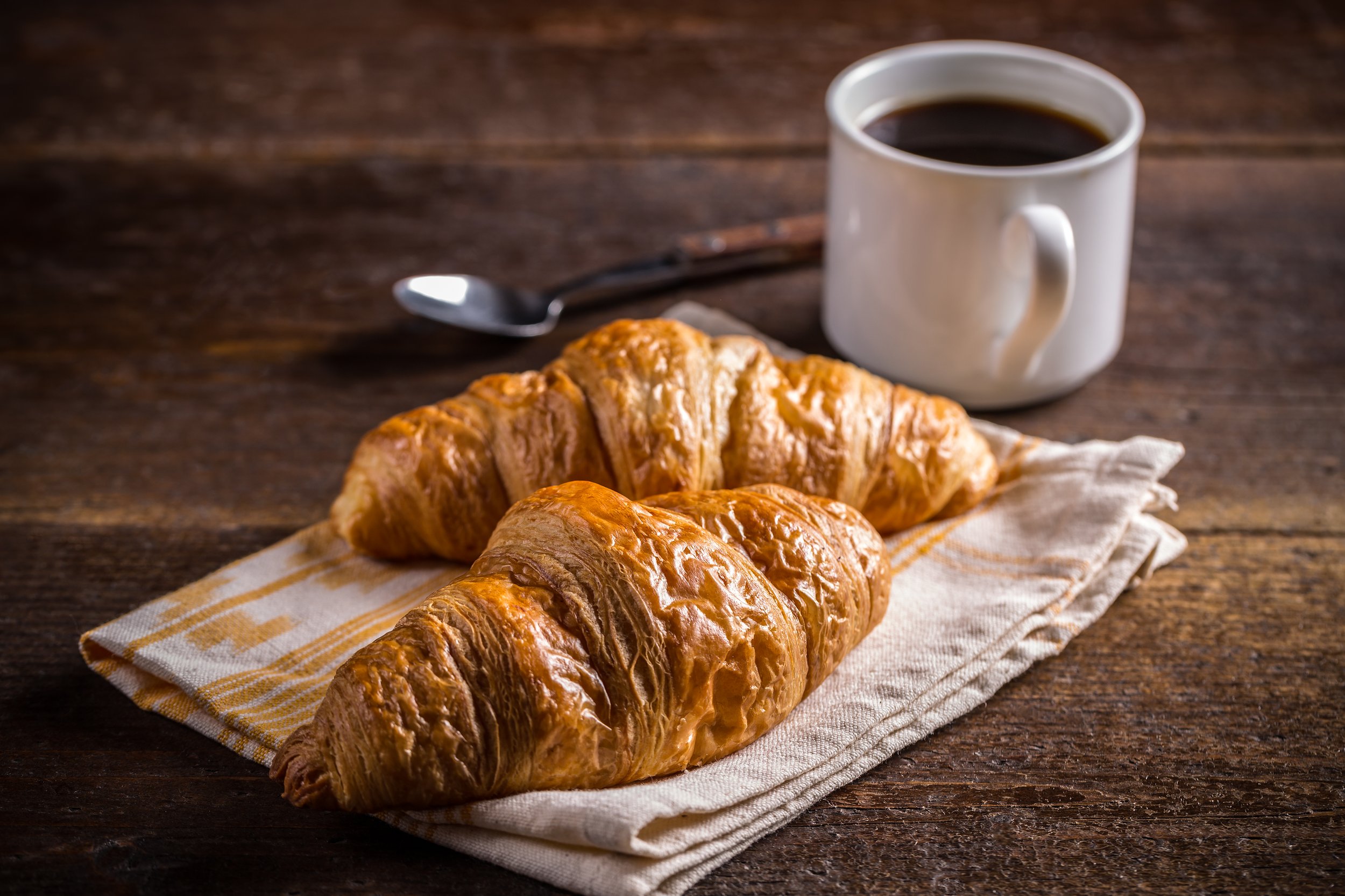 Two croissants on a napkin with a cup of black coffee on a wooden table.