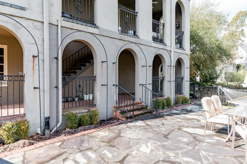Exterior view of a two-story building with arches and balconies, stone patio, and outdoor seating area.