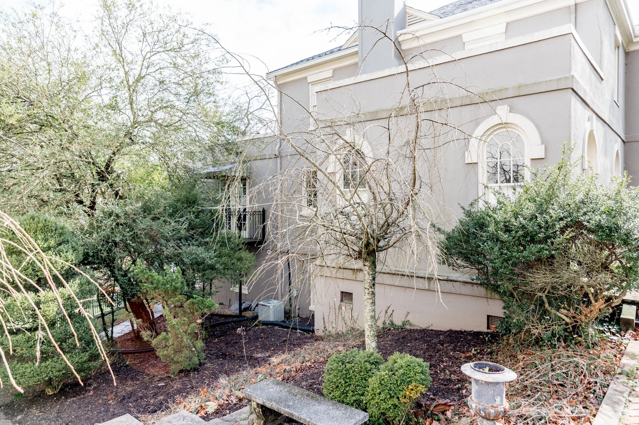 Exterior of a beige stucco house with arched windows surrounded by winter trees and shrubs in the yard.