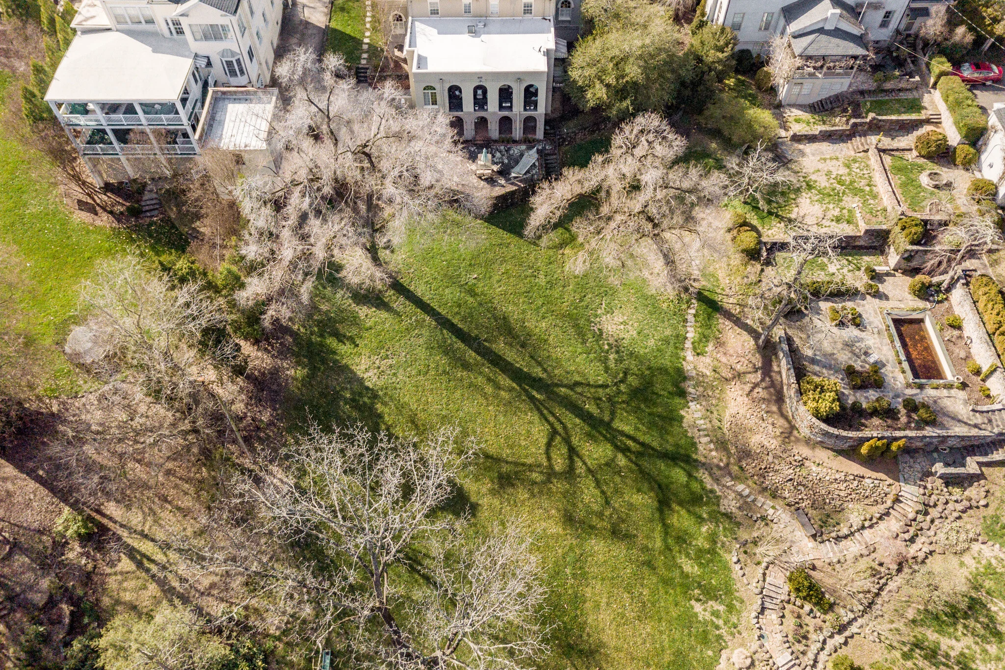 Aerial view of backyard with lawns, pathways, bare trees, and adjacent houses.
