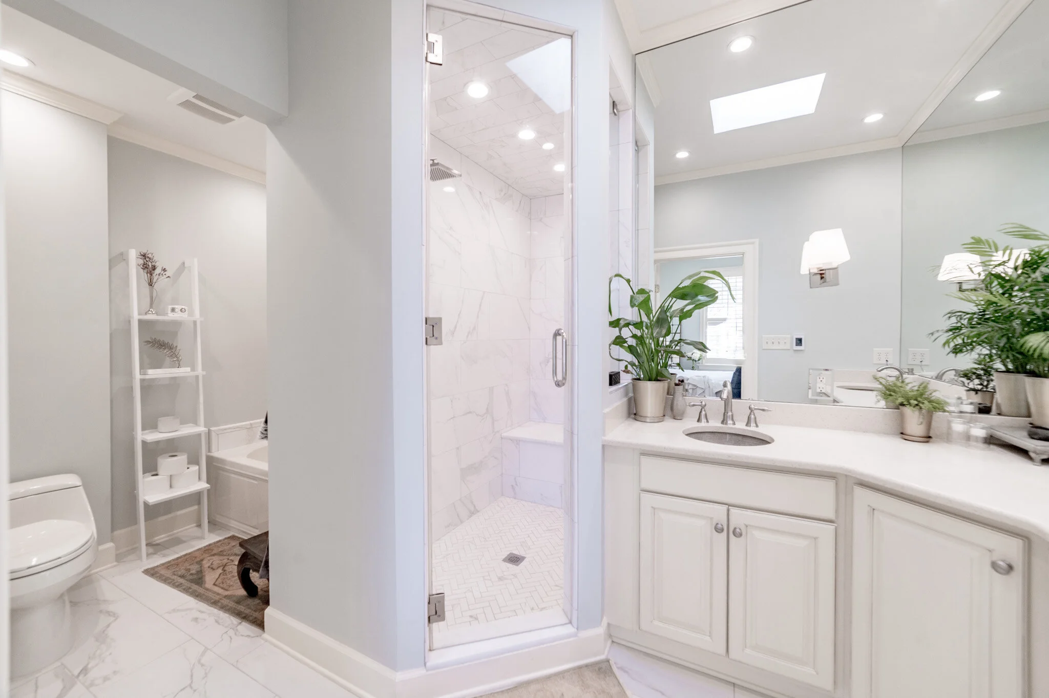 Modern bathroom interior with glass shower, vanity with sink, potted plants, toilet, and white shelving.