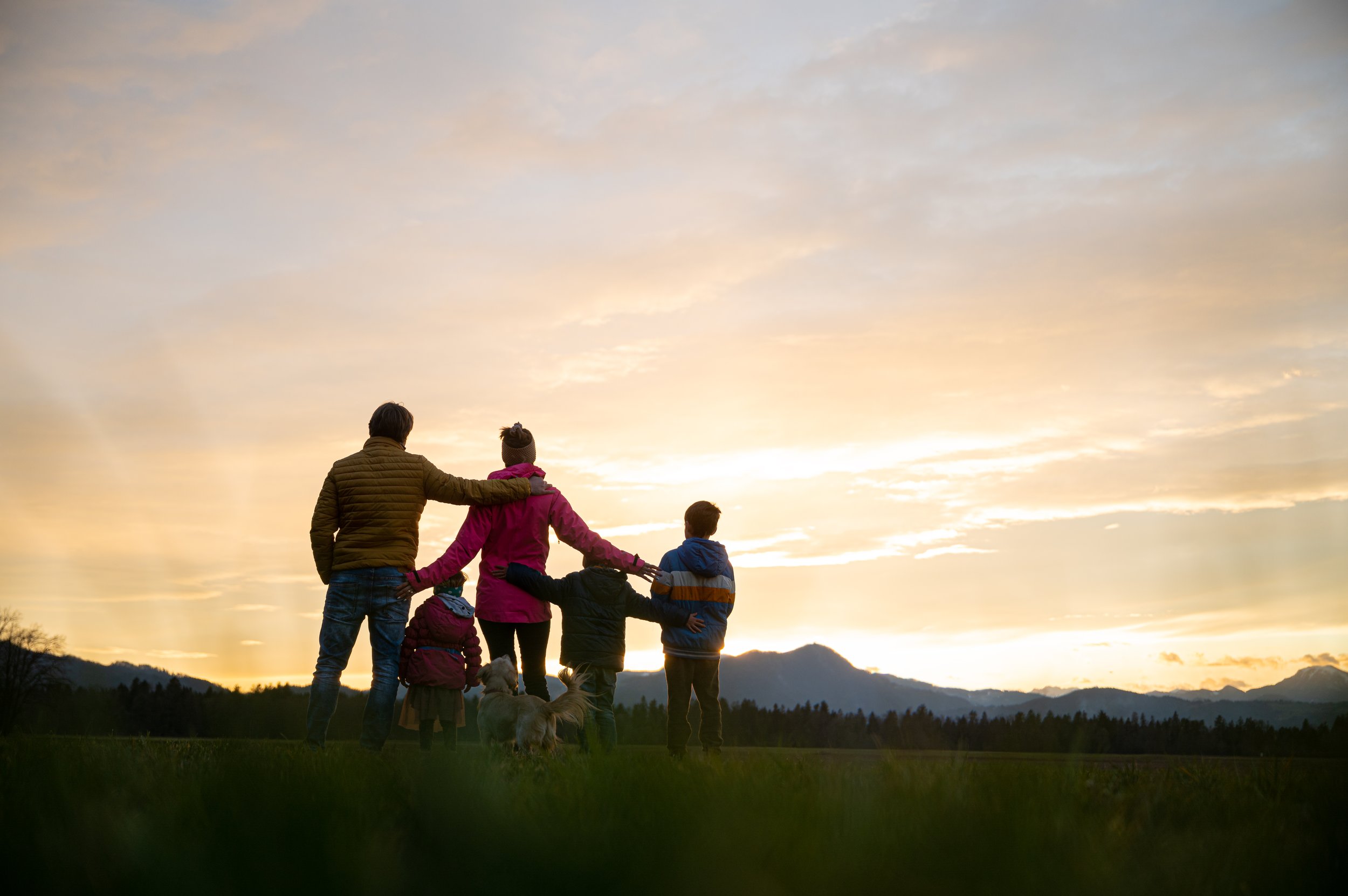 Family with children and dog standing in field at sunset
