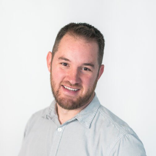Person with short hair and a beard smiling, wearing a light-colored shirt against a plain background.