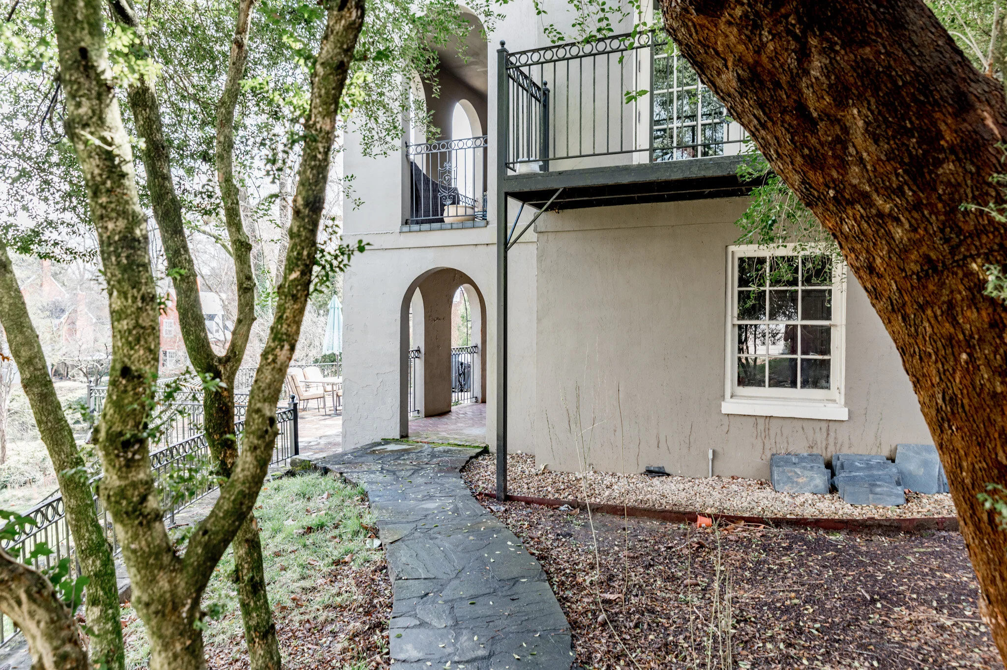 Outdoor view of a residential building with arches, metal railings, and a stone walkway surrounded by trees and grass.