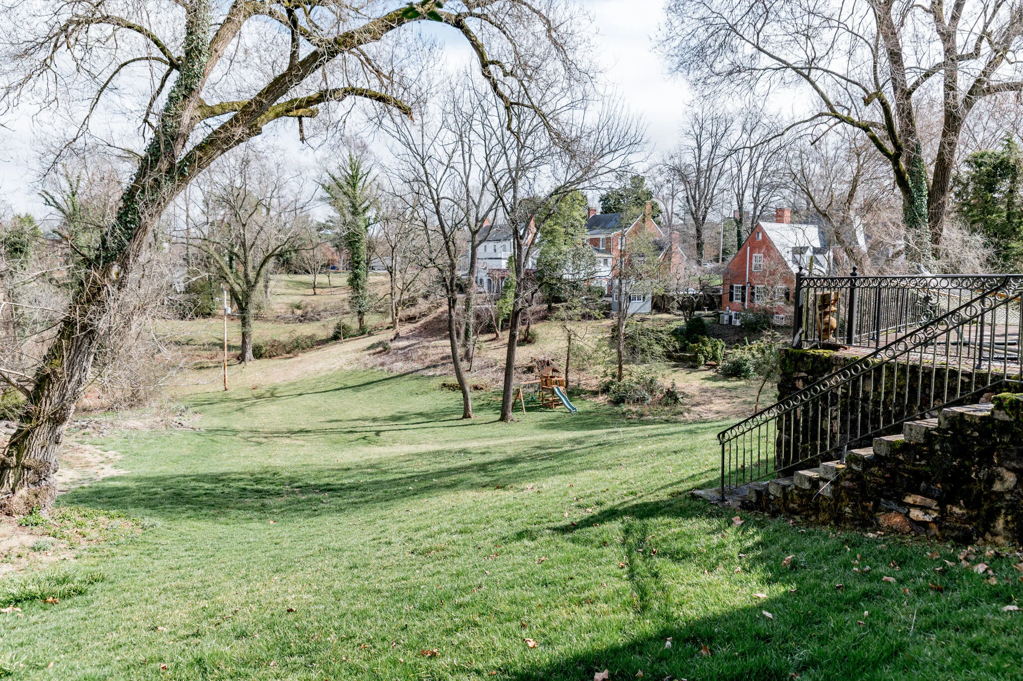 Landscape with grassy lawn, bare trees, residential houses, swing set, and stone staircase with metal railing.