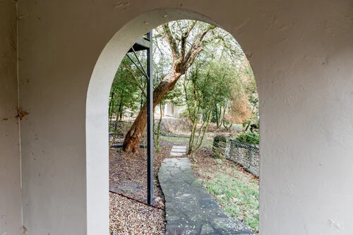 View through an arched doorway onto a garden path, surrounded by trees and greenery.