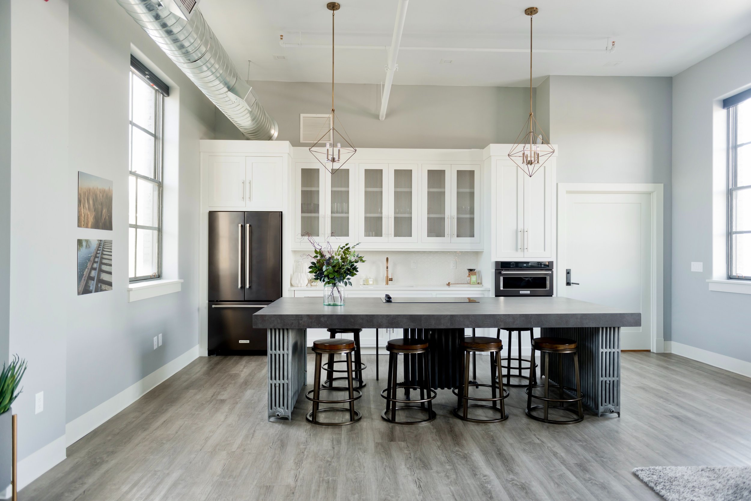 Modern kitchen with white cabinets, large island with bar stools, pendant lights, and stainless steel appliances.