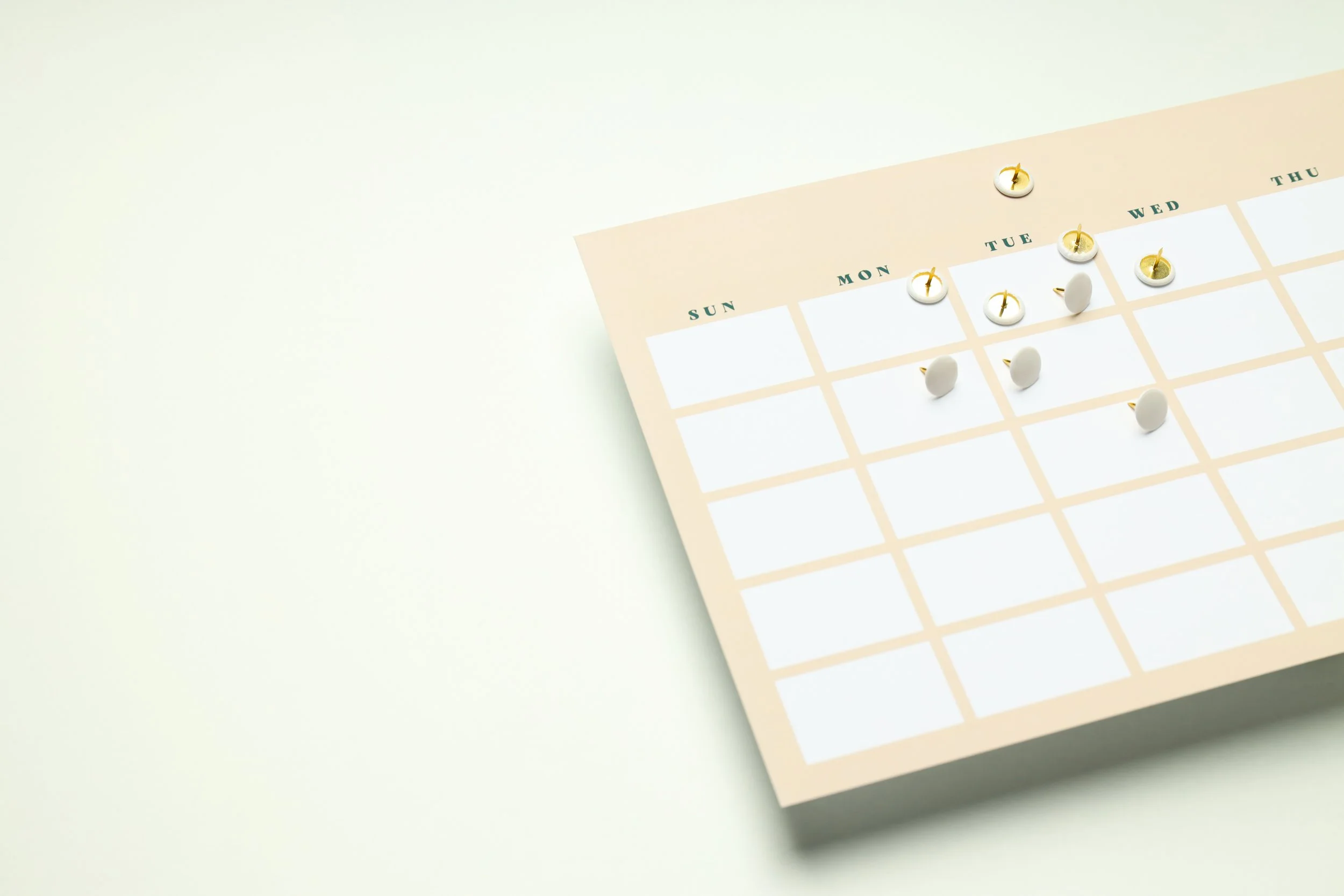 Minimalist calendar with push pins on a light background, marking days of the week from Sunday to Thursday.