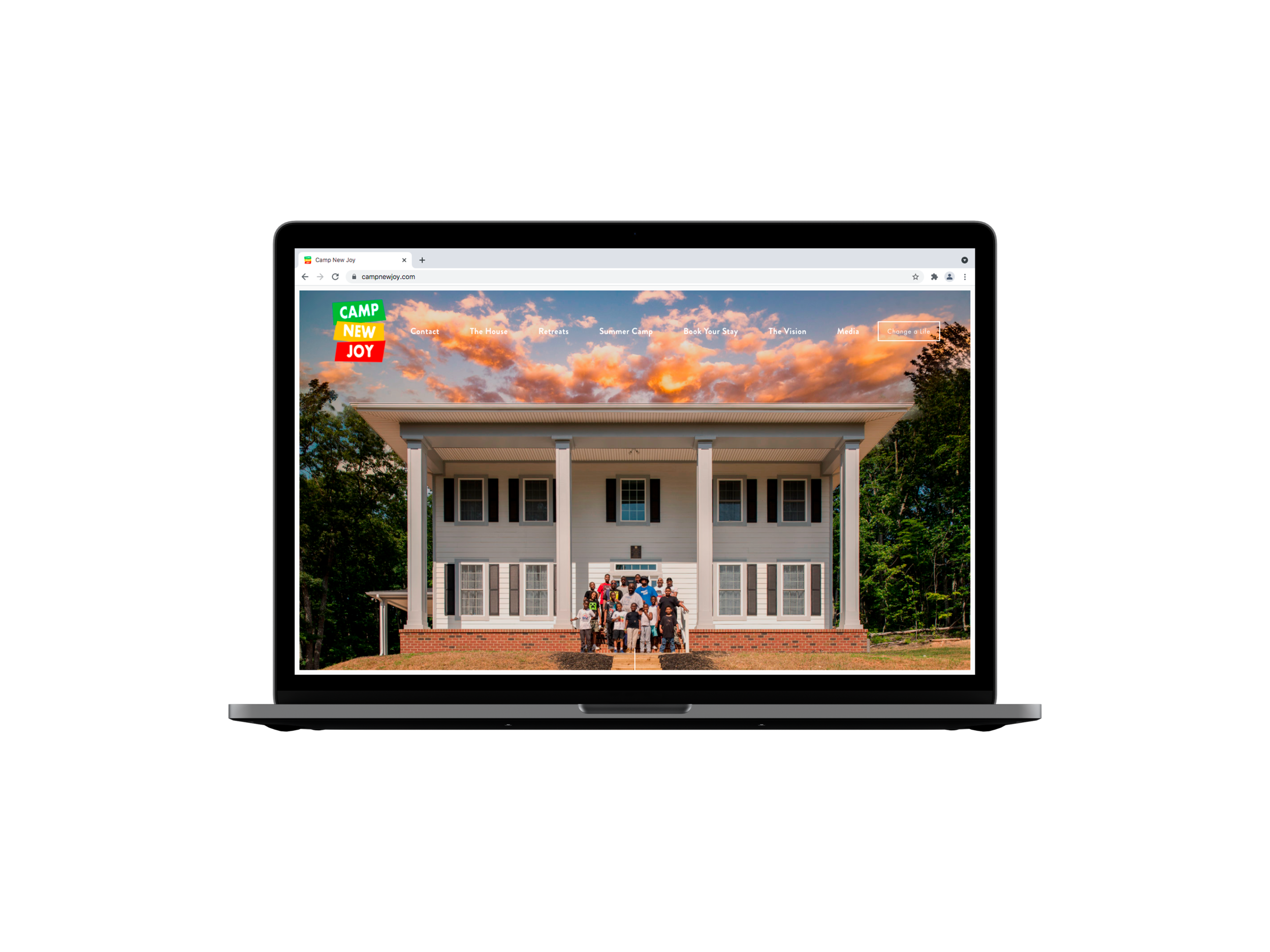 Laptop displaying a website with a photo of a large house and several people in front. "Camp New Joy" is in the corner of the screen. The website menu is visible with options like Contact, The House, Rentals, and Summer."