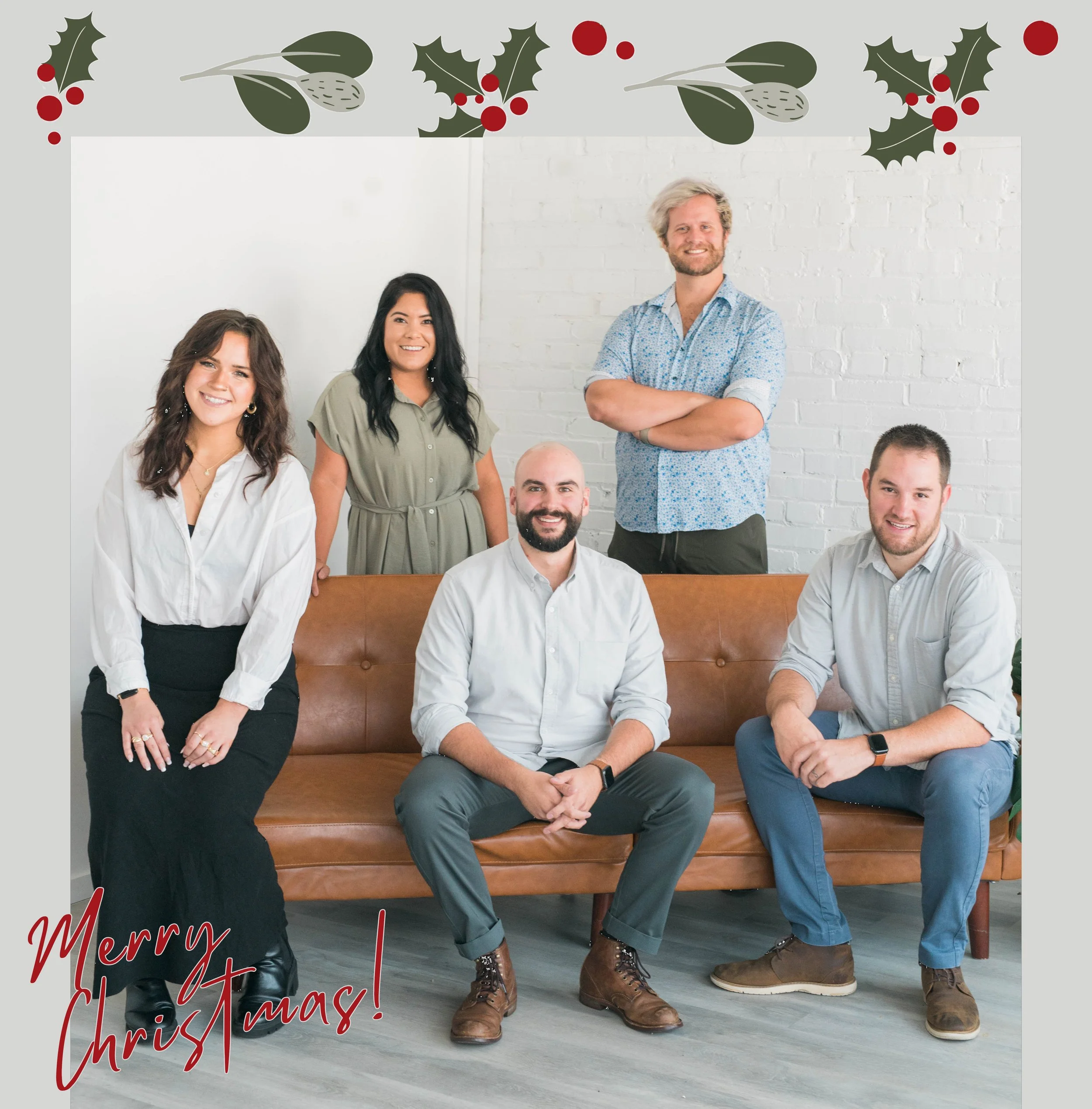 Group of five people in casual attire posing on a brown couch with a holiday theme; decorated with holly and "Merry Christmas!" text.