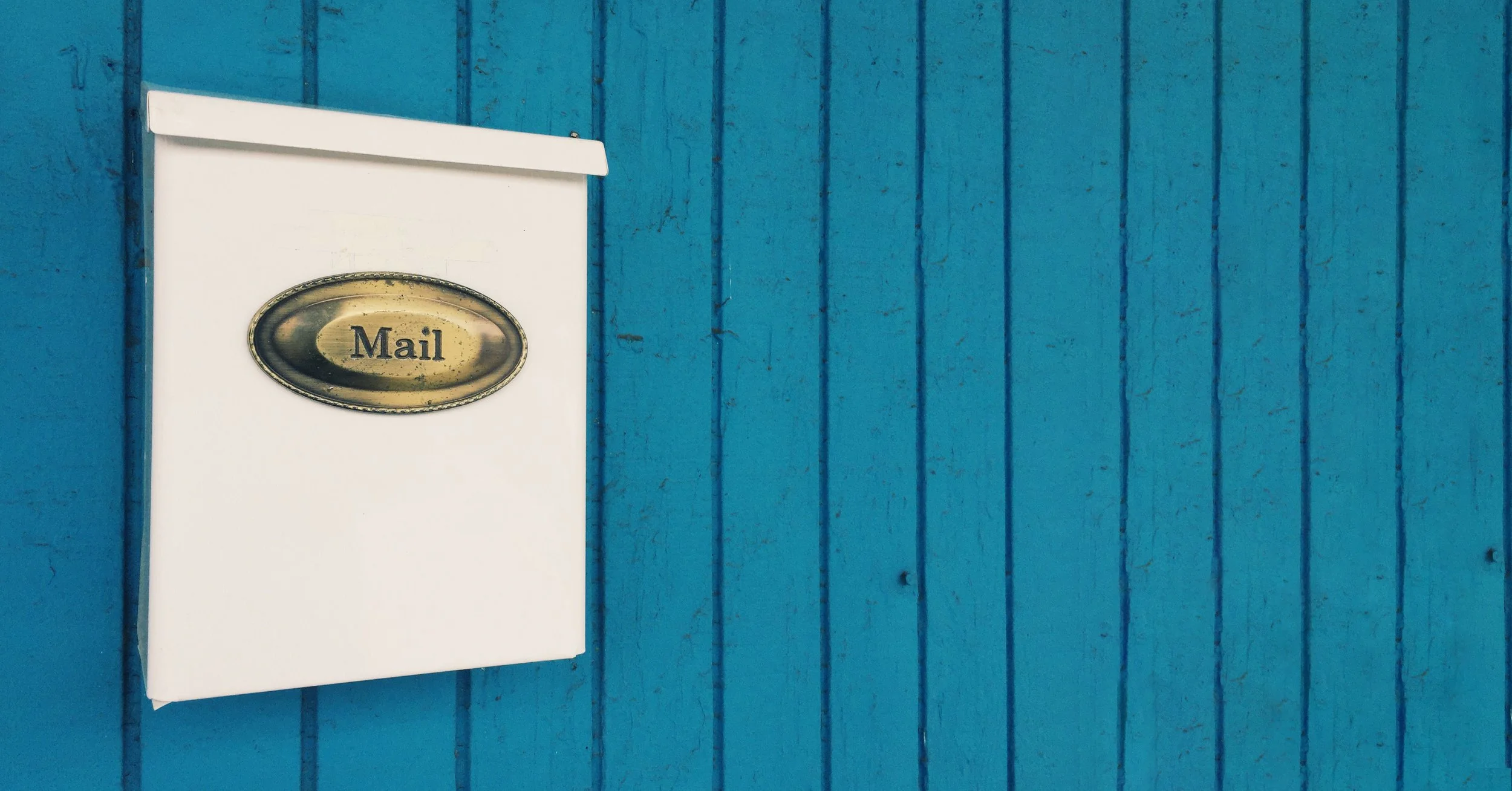 White mailbox with "Mail" sign on a blue wooden wall