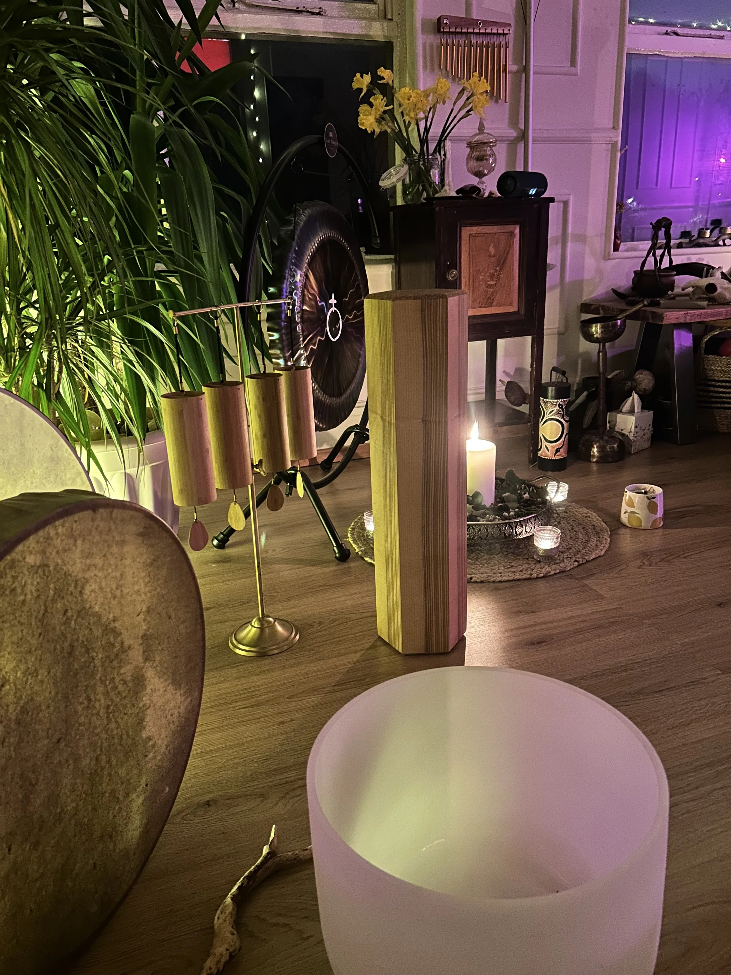 Variet of soundhealing equipment including chimes, drum and crystal bowls in a candle lit cosy and colourful room