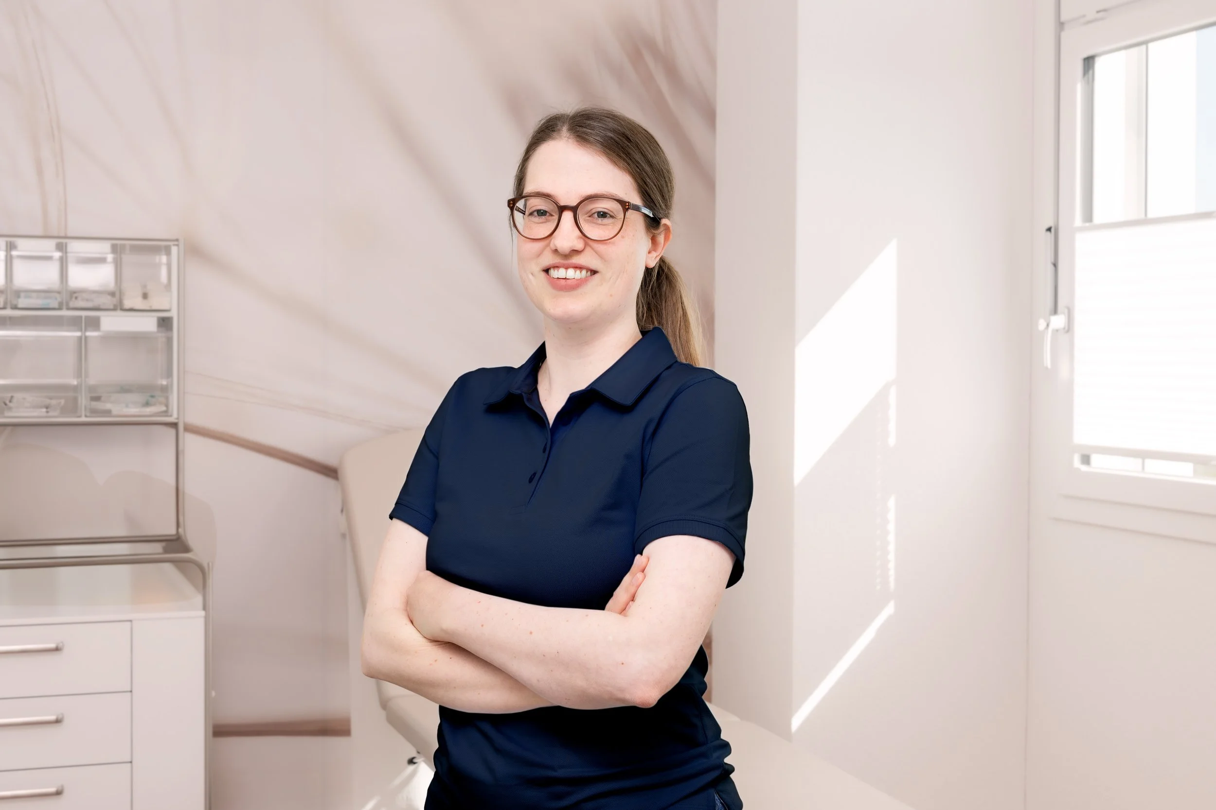 Frau mit Brille, langen braunen Haaren und dunklem Oberteil vor blauem Hintergrund.