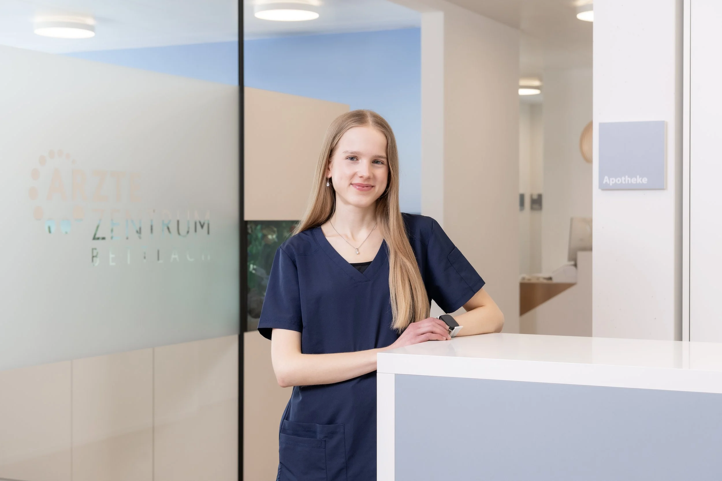 Porträt einer jungen Frau mit langen, blonden Haaren und blauem Oberteil auf blauem Hintergrund.