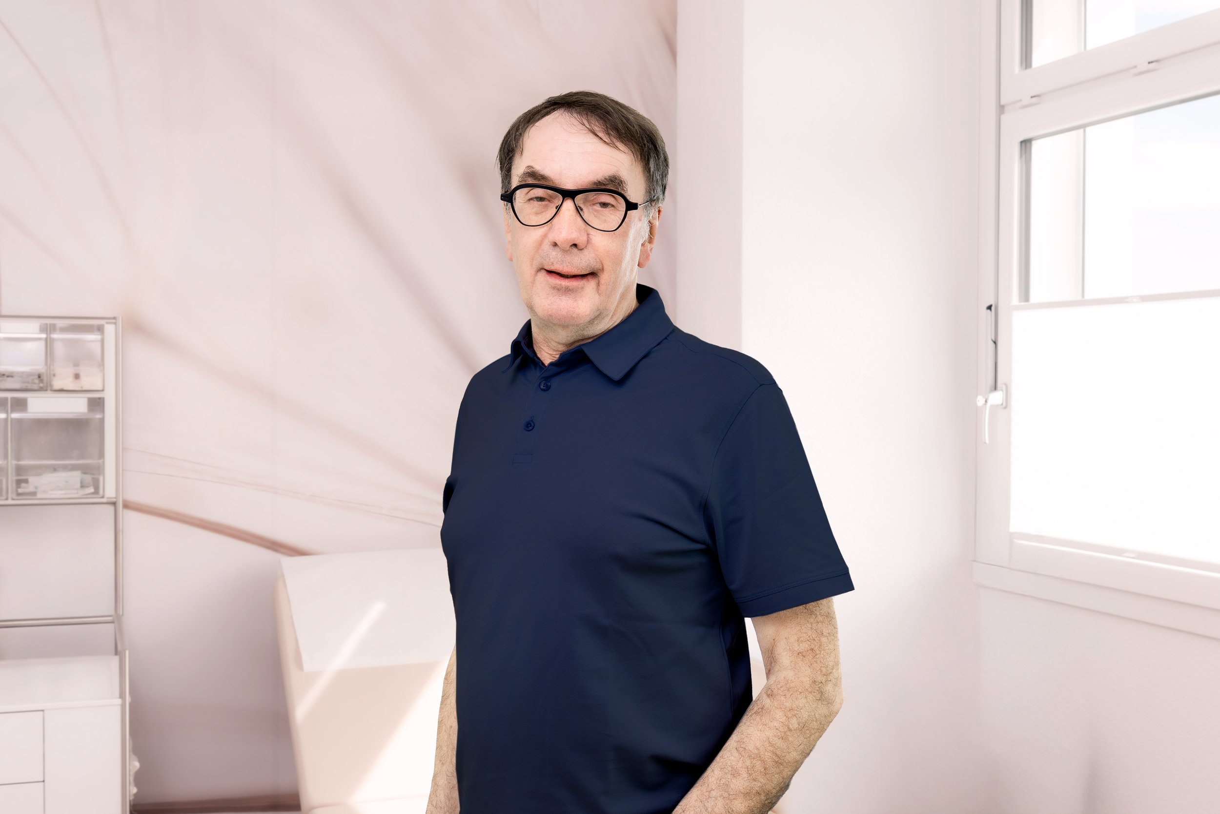 Porträt eines älteren Mannes mit Brille und blauer Kleidung vor blauem Hintergrund.