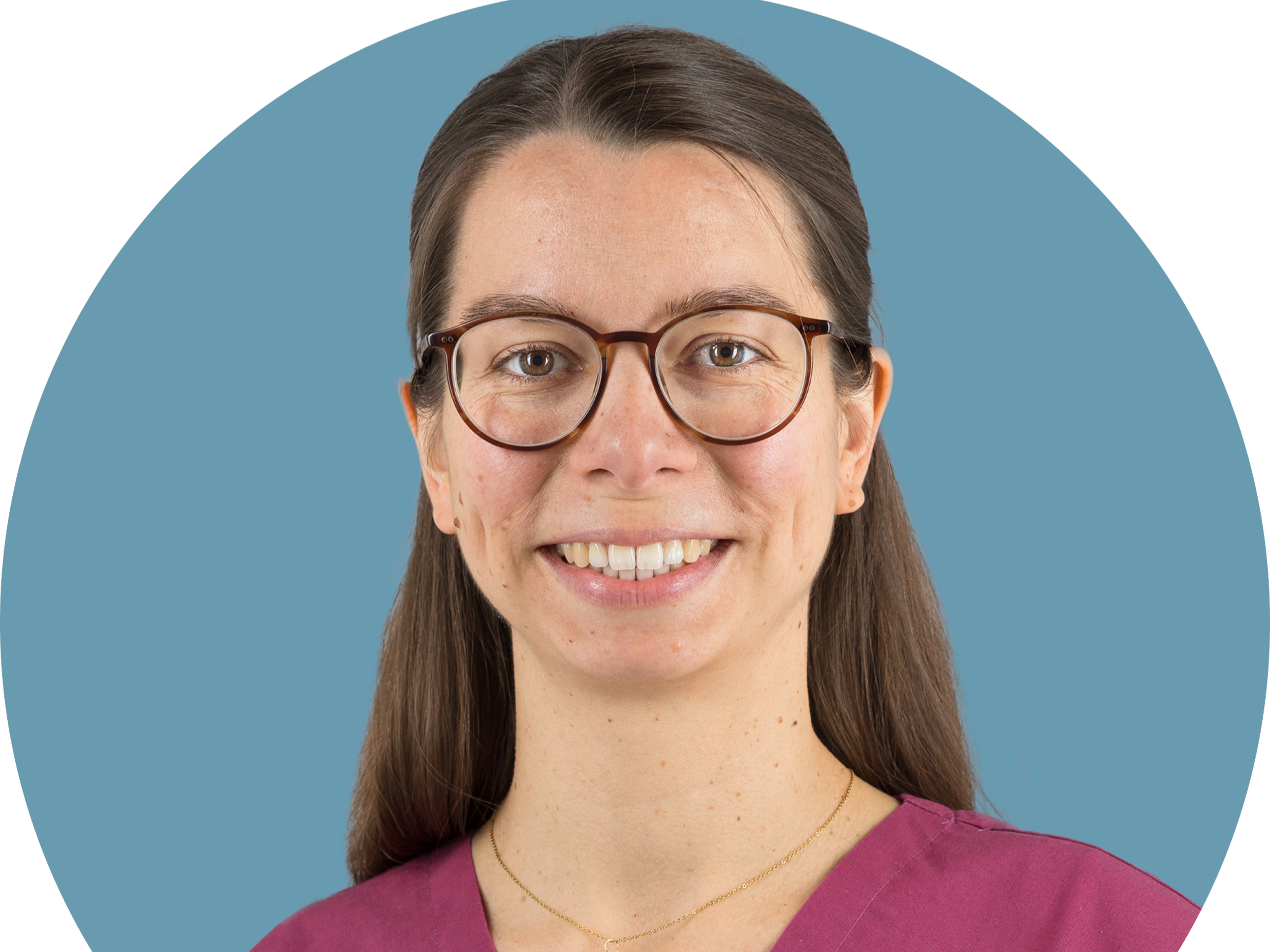 Frau mit Brille in medizinischer Kleidung vor blauem Hintergrund.