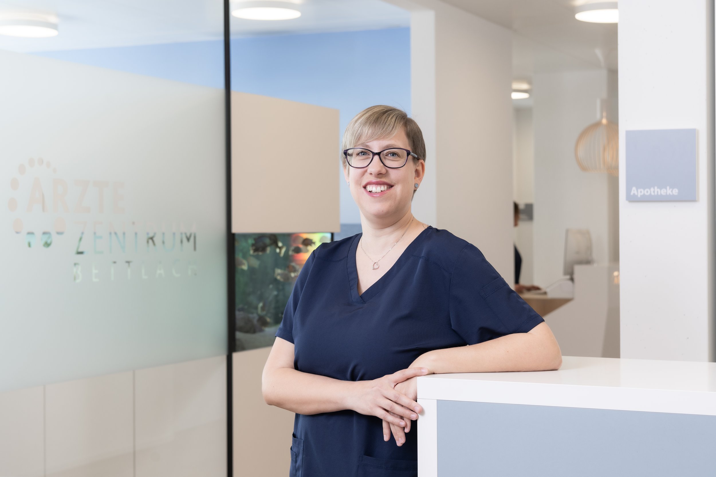 Eine Person mit Brille und kurzem Haar lächelt vor einem blauen Hintergrund.