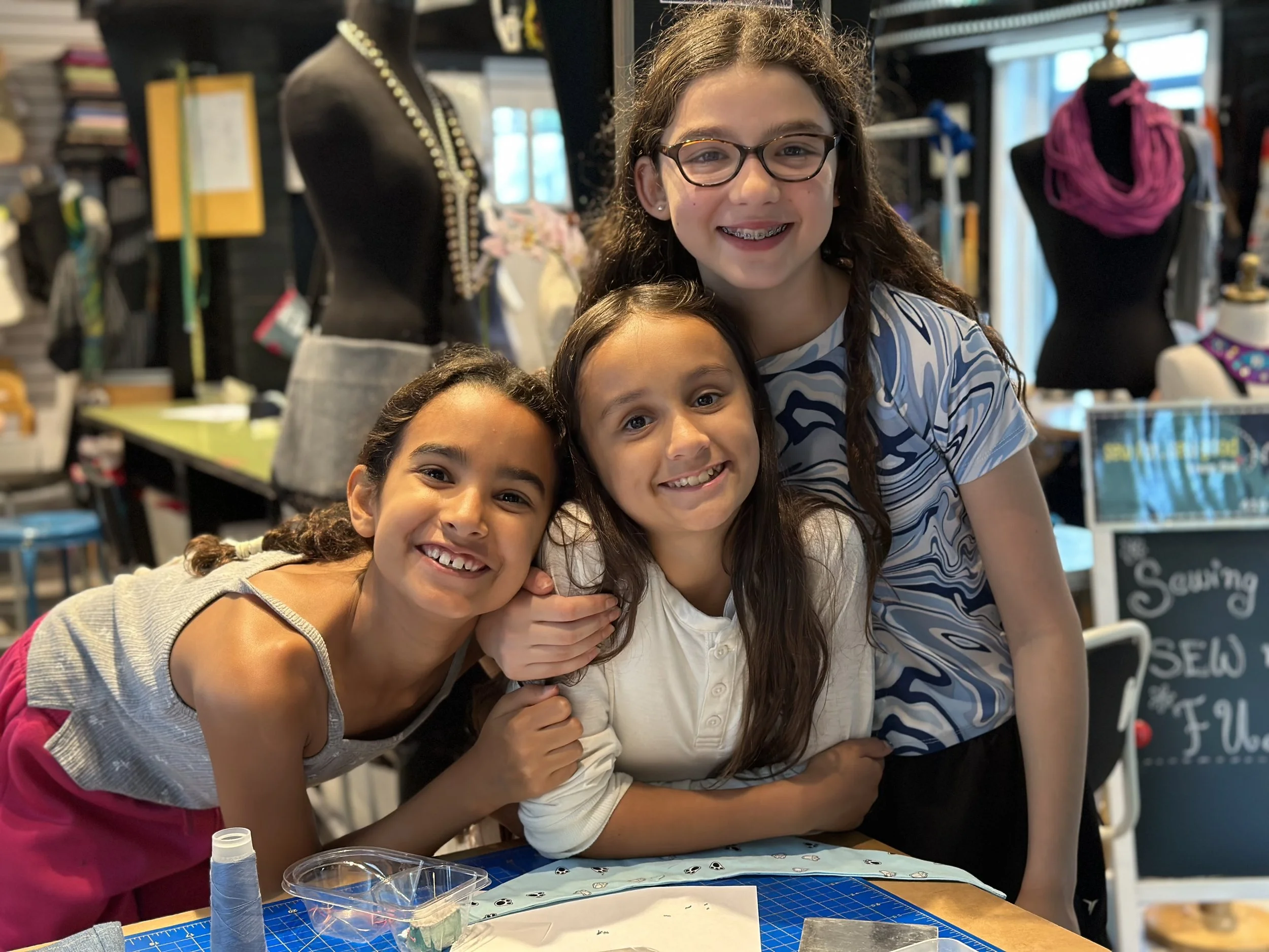 Three young girls happily hanging out in a cool sewing studio where they get to be creative and make friends.