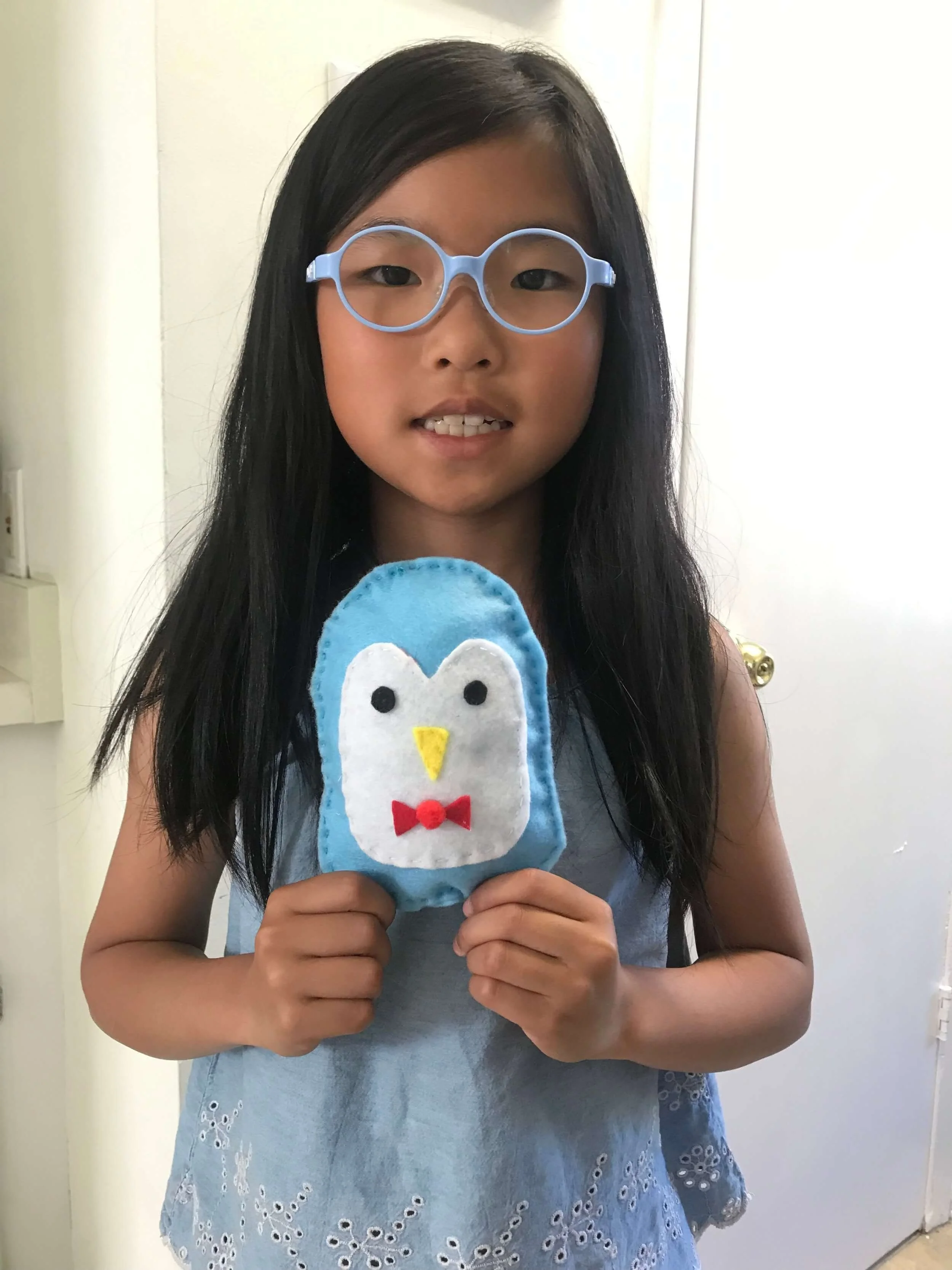 A young girl with long dark hair and glasses shows her sewing project, a stuffie